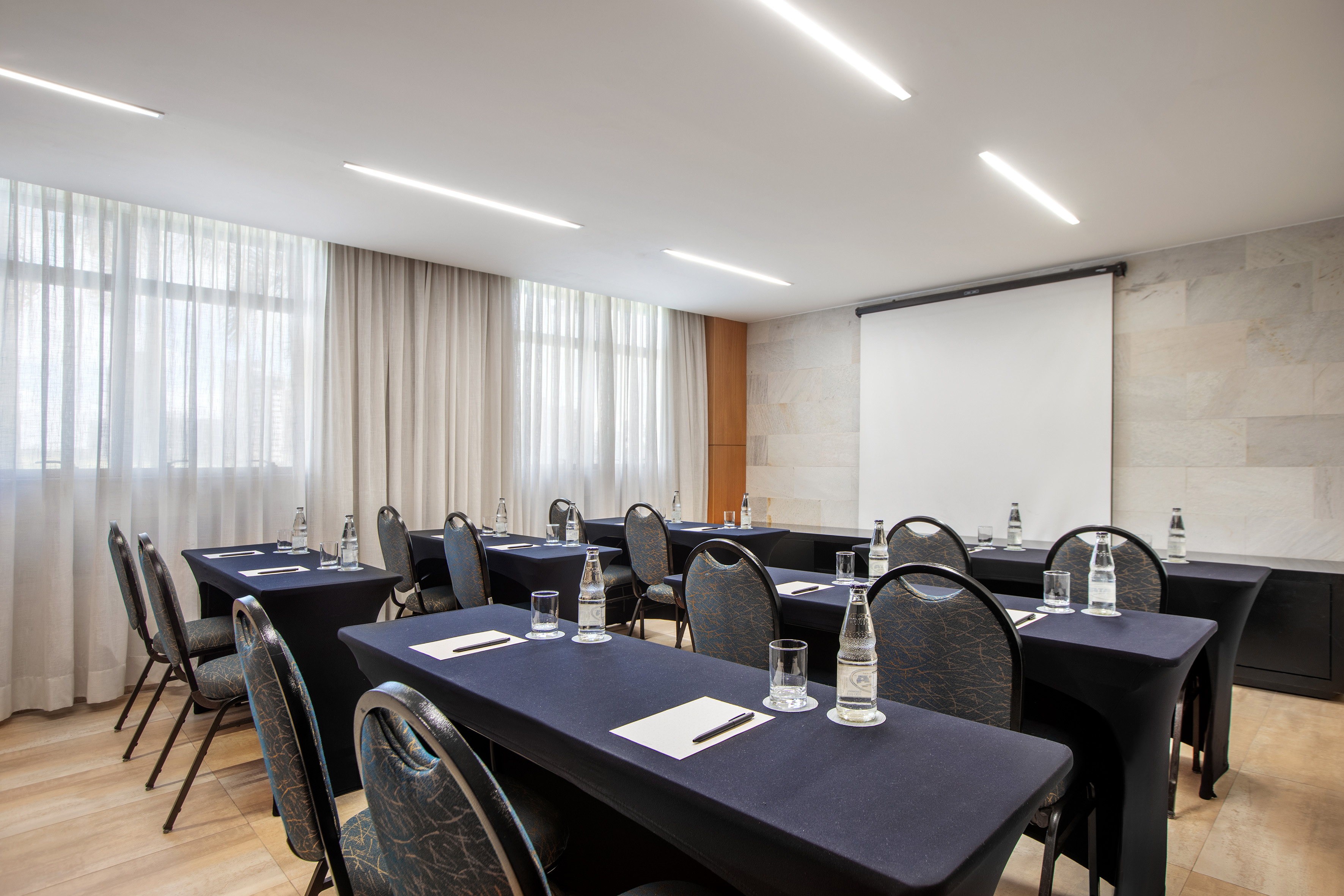 Modern conference room with tables, chairs, projector screen, and large windows.