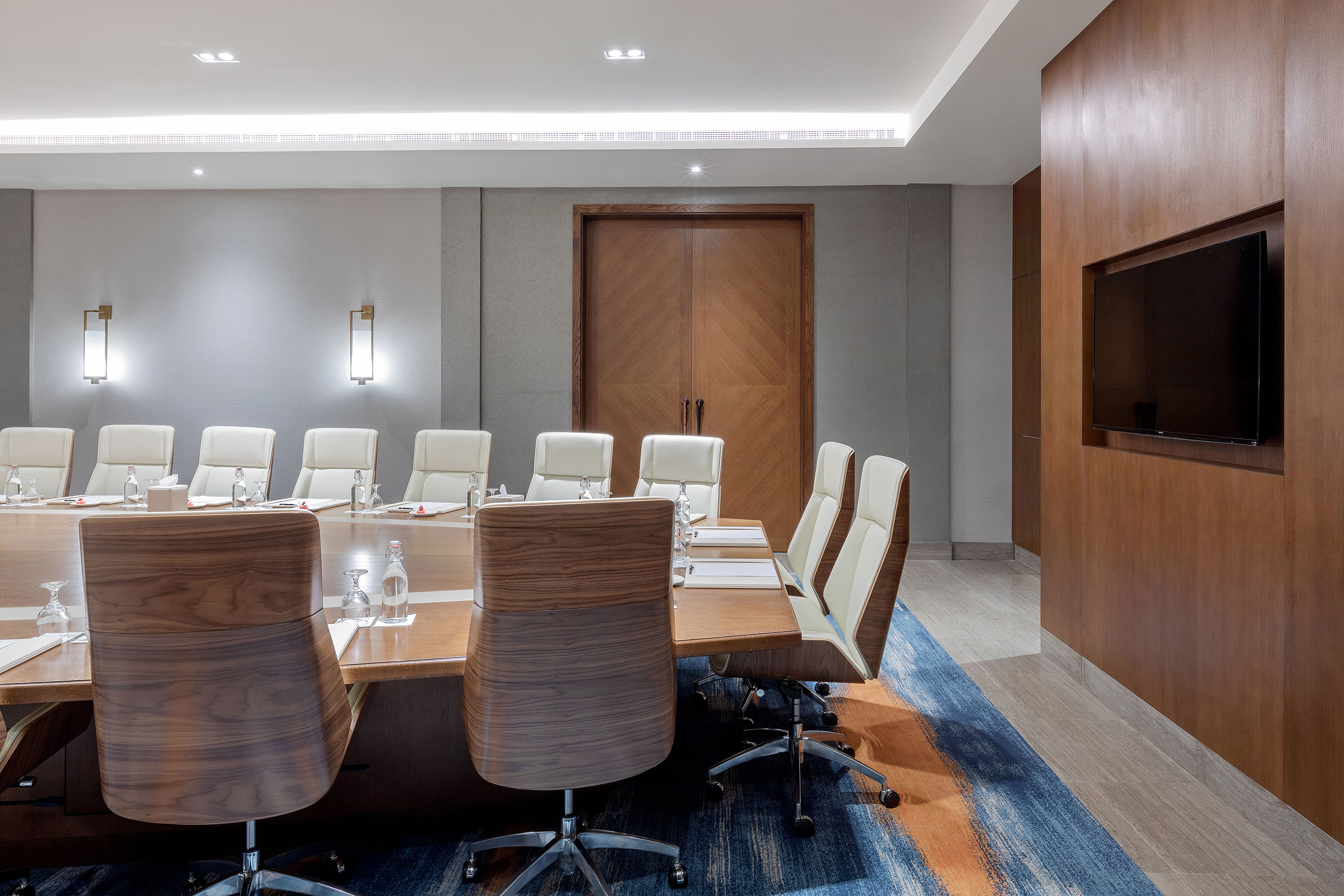 Modern boardroom with wooden conference table, executive chairs, and TV.