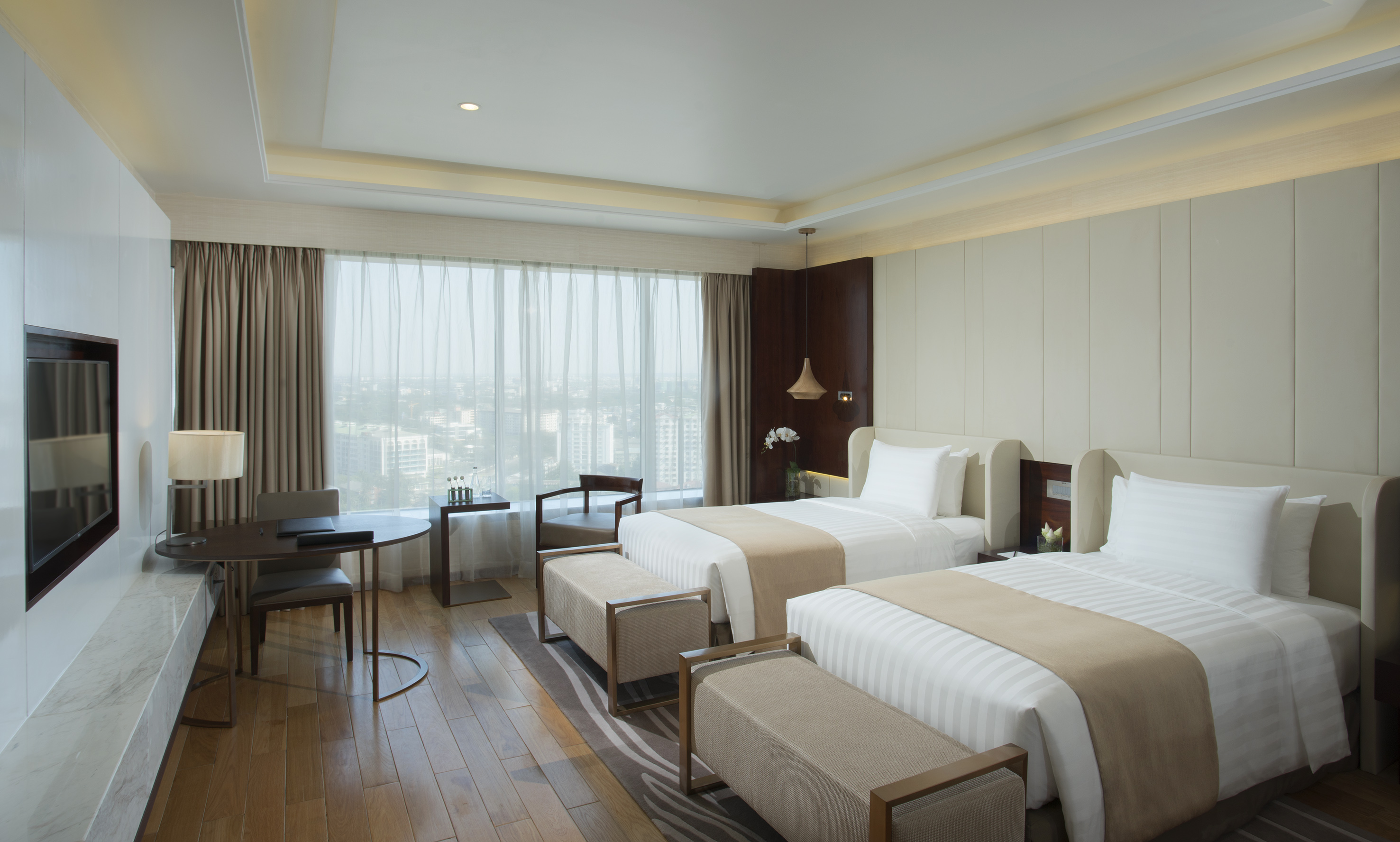 Modern twin bed hotel room with city view, desk, and elegant decor.
