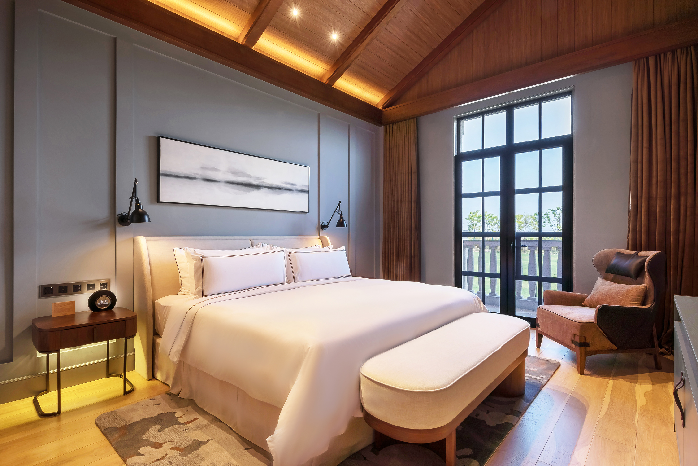 Modern hotel bedroom with vaulted wood ceiling, large bed, and balcony.