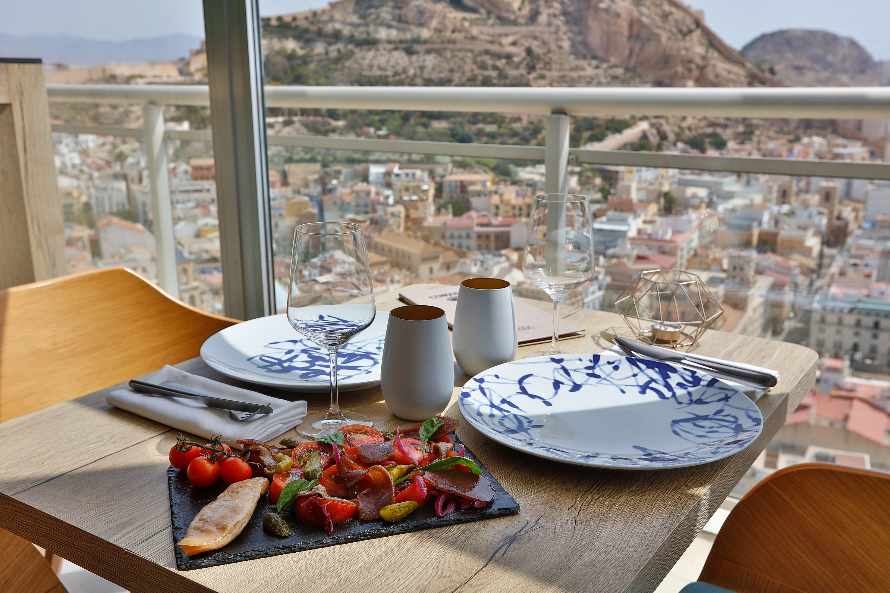 Restaurant balcony dining with appetizers, wine, city, and mountain view.