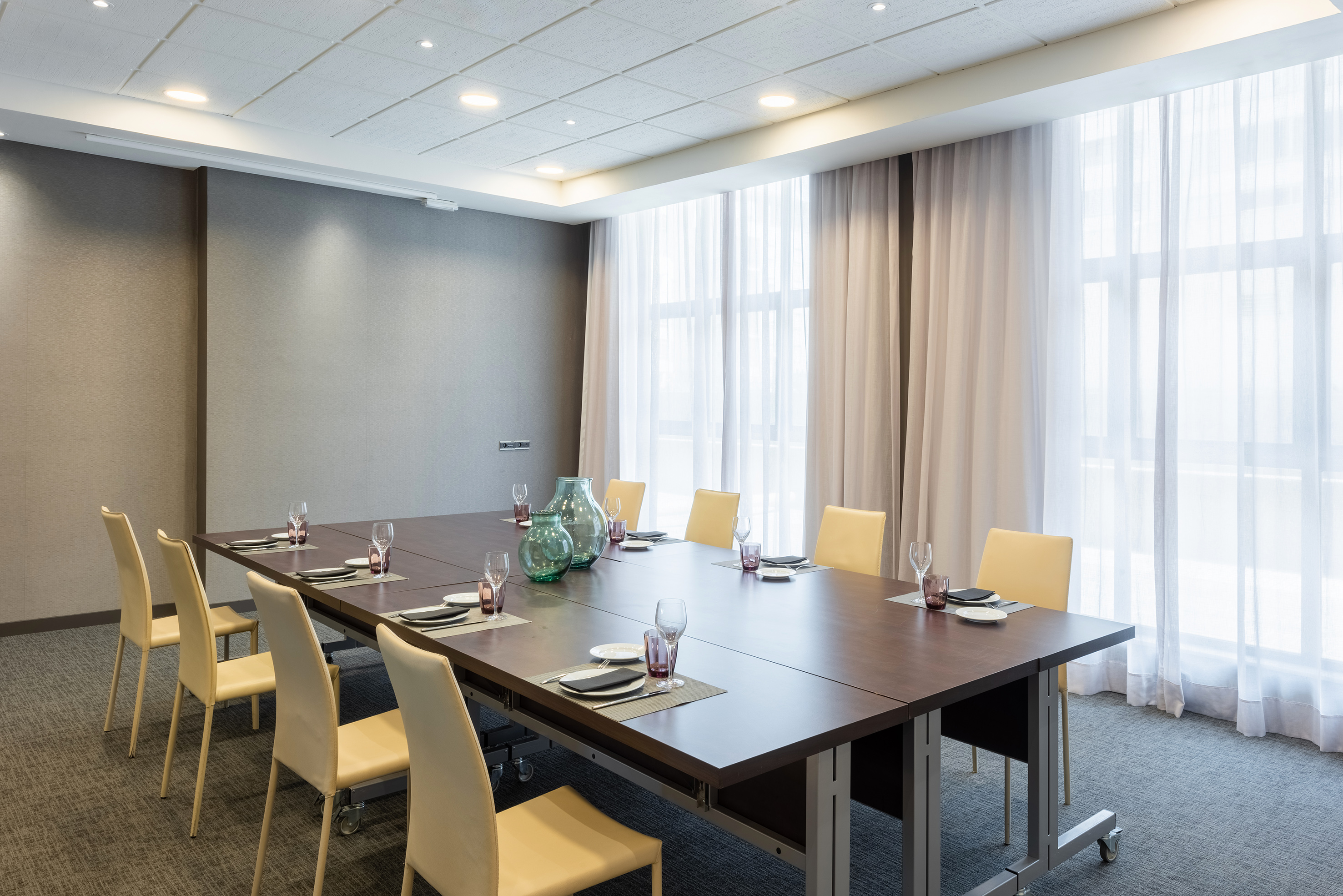Modern conference room with long table, light chairs, and sheer window light.