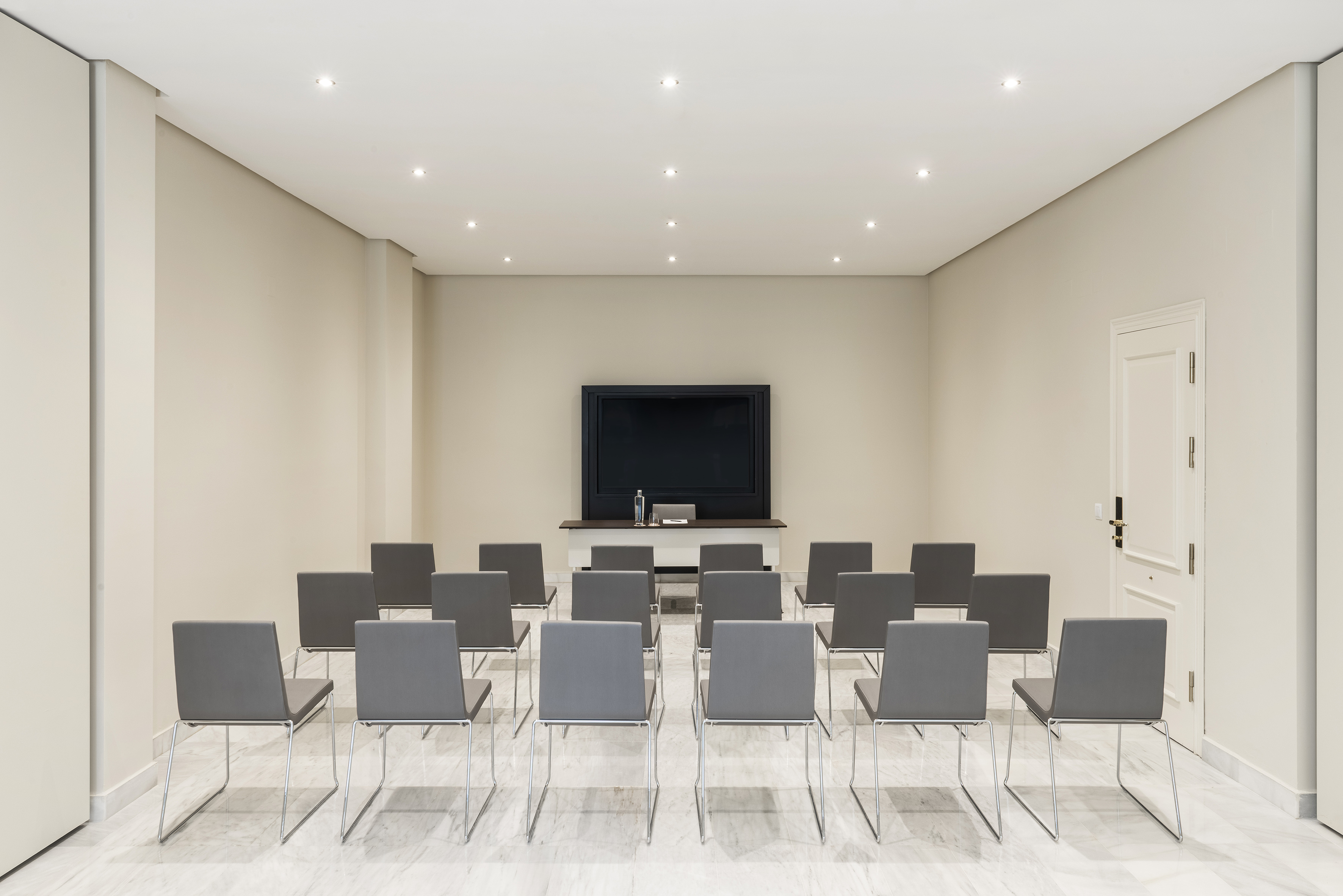 Modern meeting room with gray chairs, large TV screen, and presentation table.