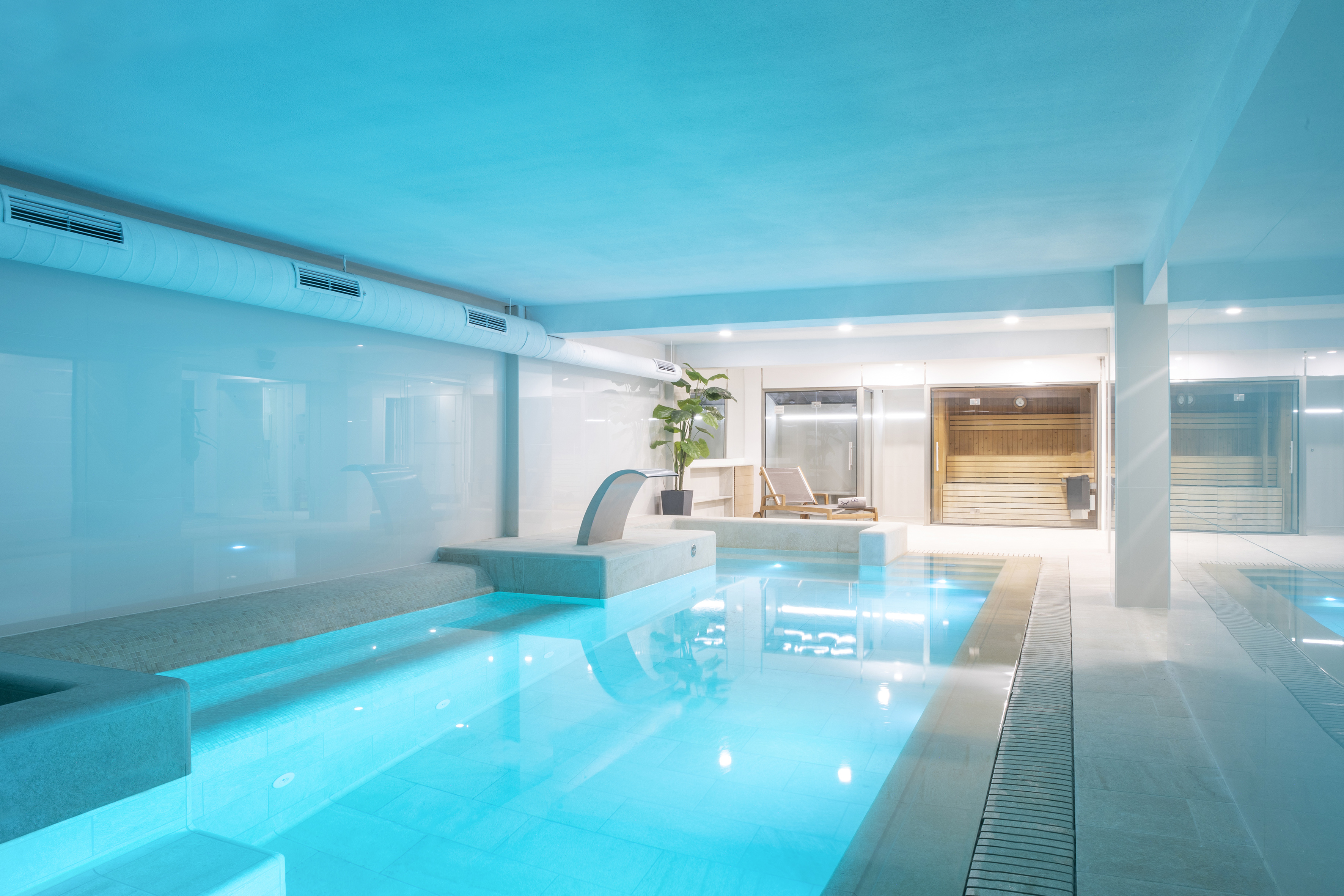 Modern hotel spa: indoor pool with waterfall, sauna, and lounge.