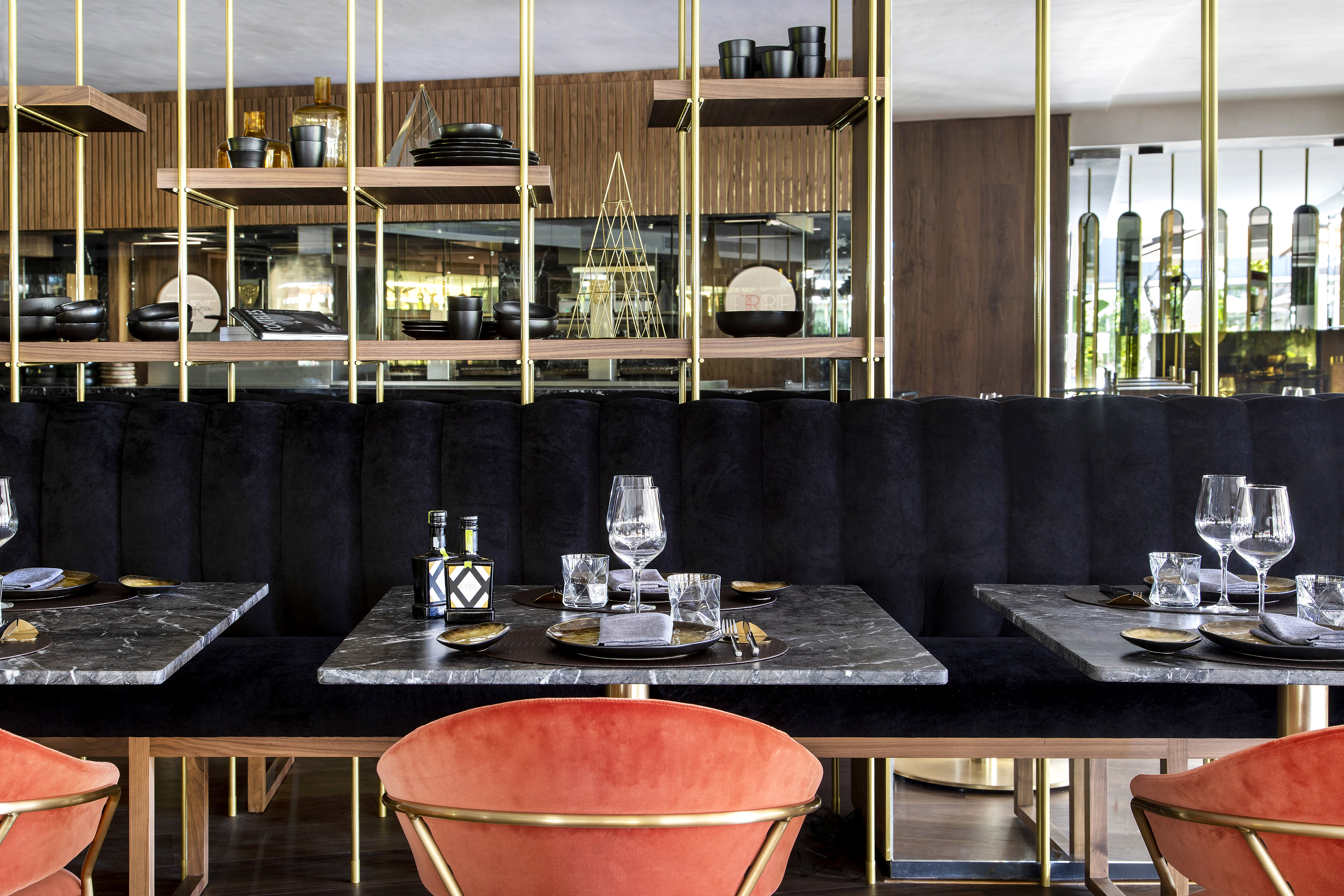 Modern restaurant dining with marble tables, black velvet banquette, and brass decor.