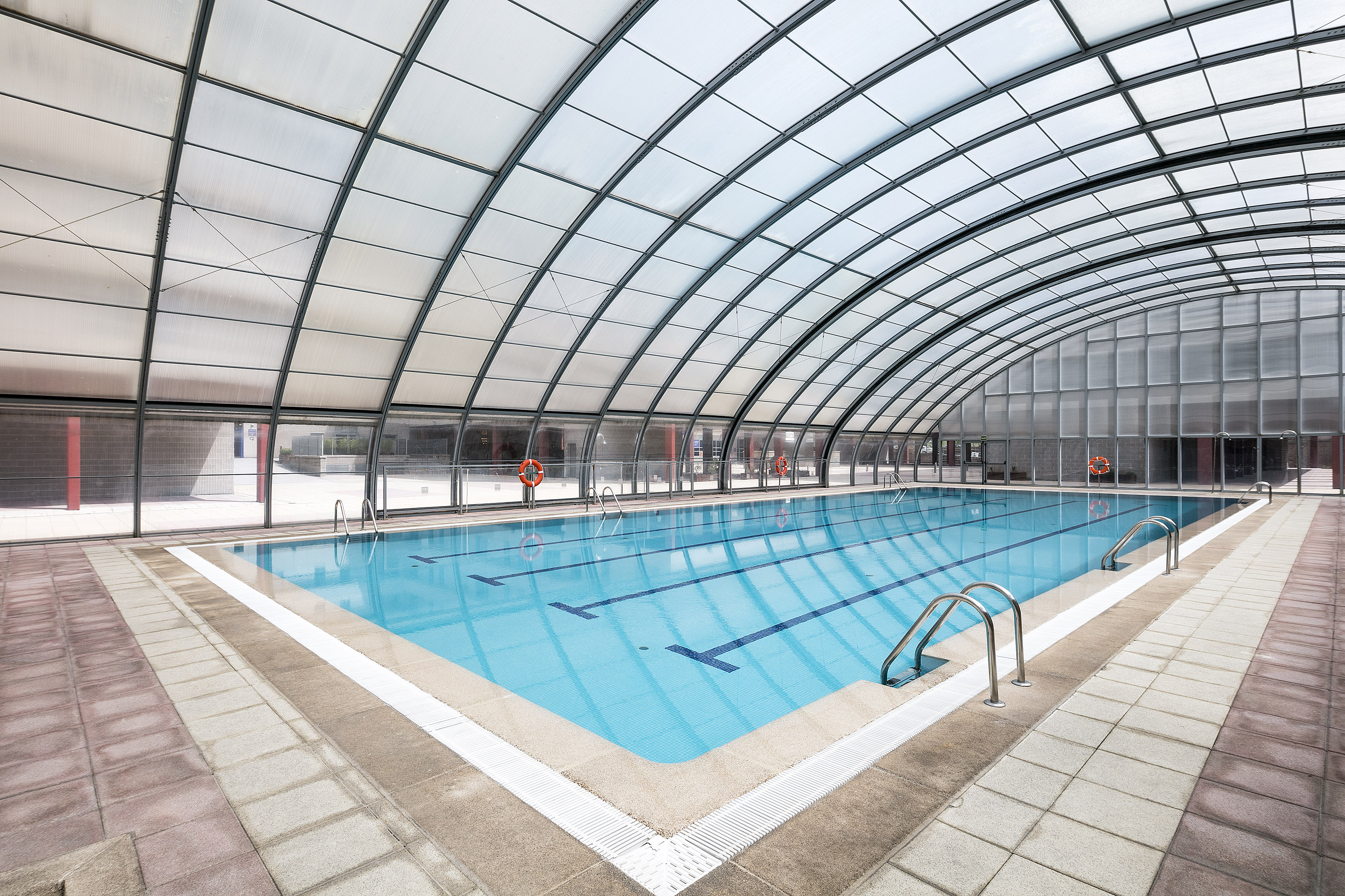 Indoor swimming pool with arched translucent roof and clear blue water.