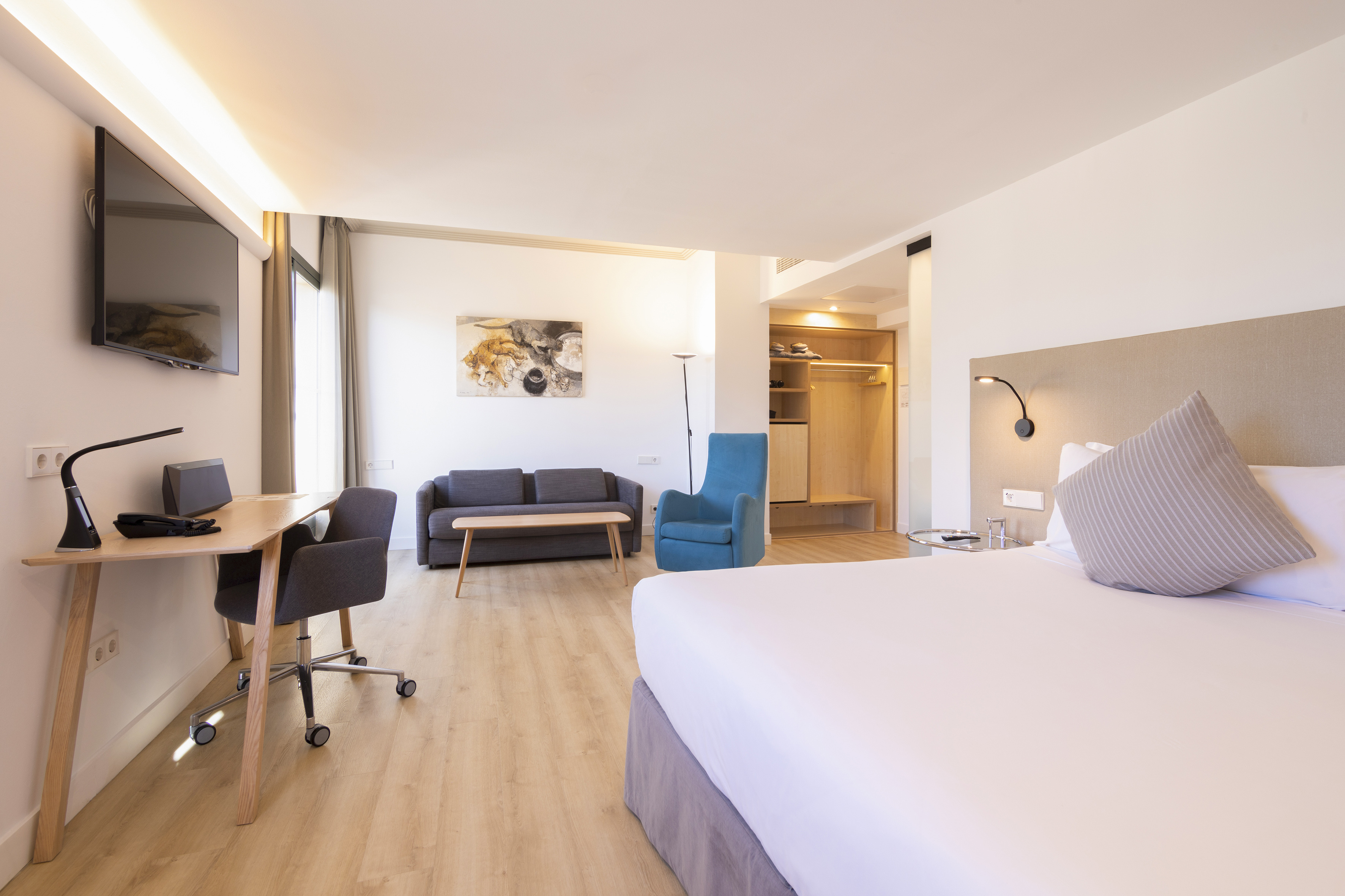 Contemporary hotel room with king bed, work desk, sofa, and open closet.