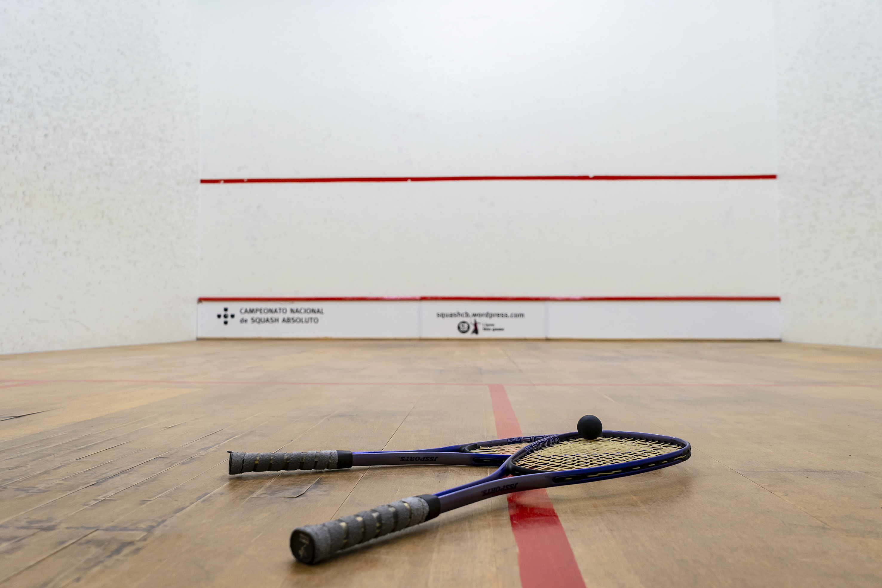Two squash rackets and ball on wooden court floor, championship backdrop.