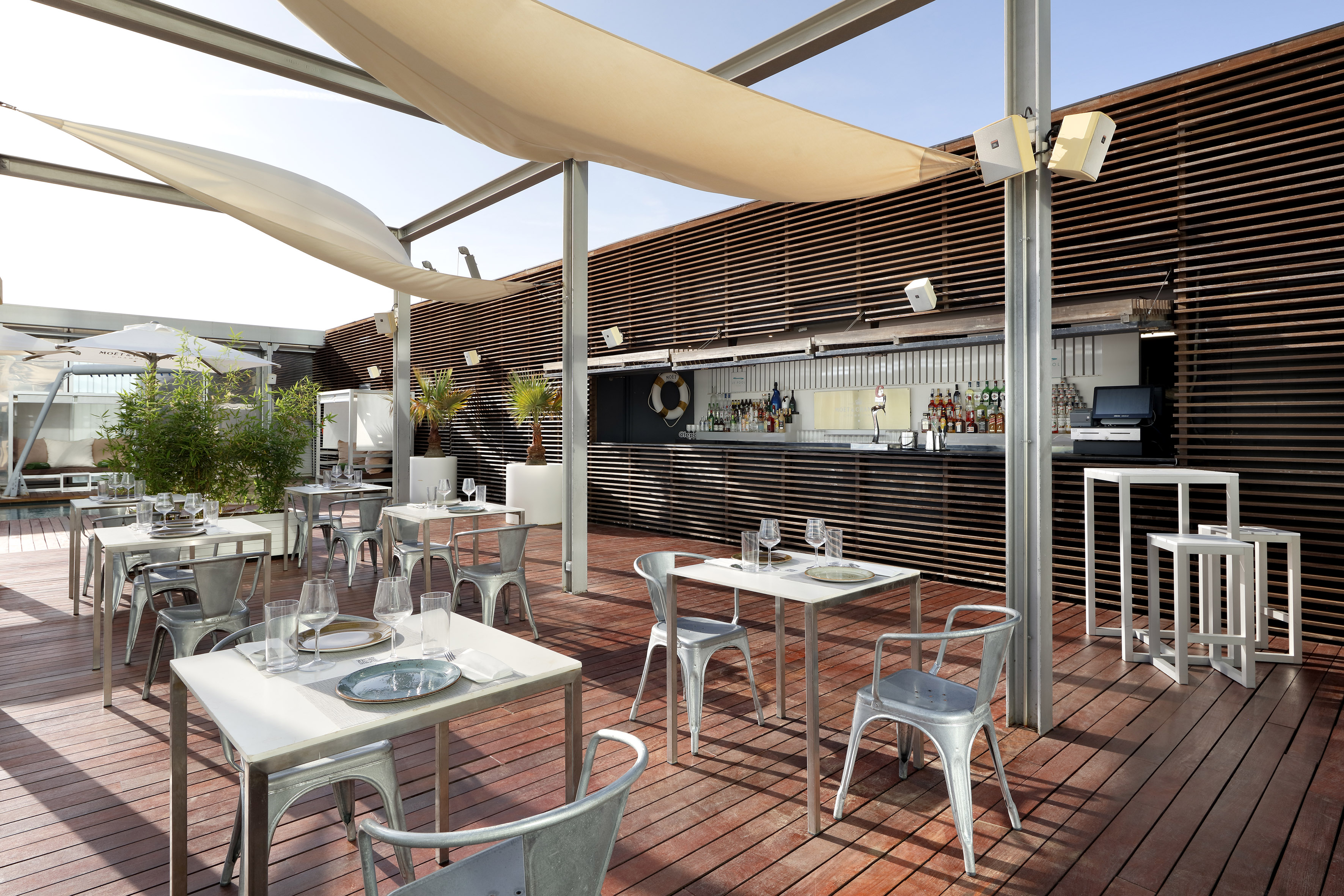 Rooftop bar and restaurant terrace with outdoor dining, wooden deck, and shade.