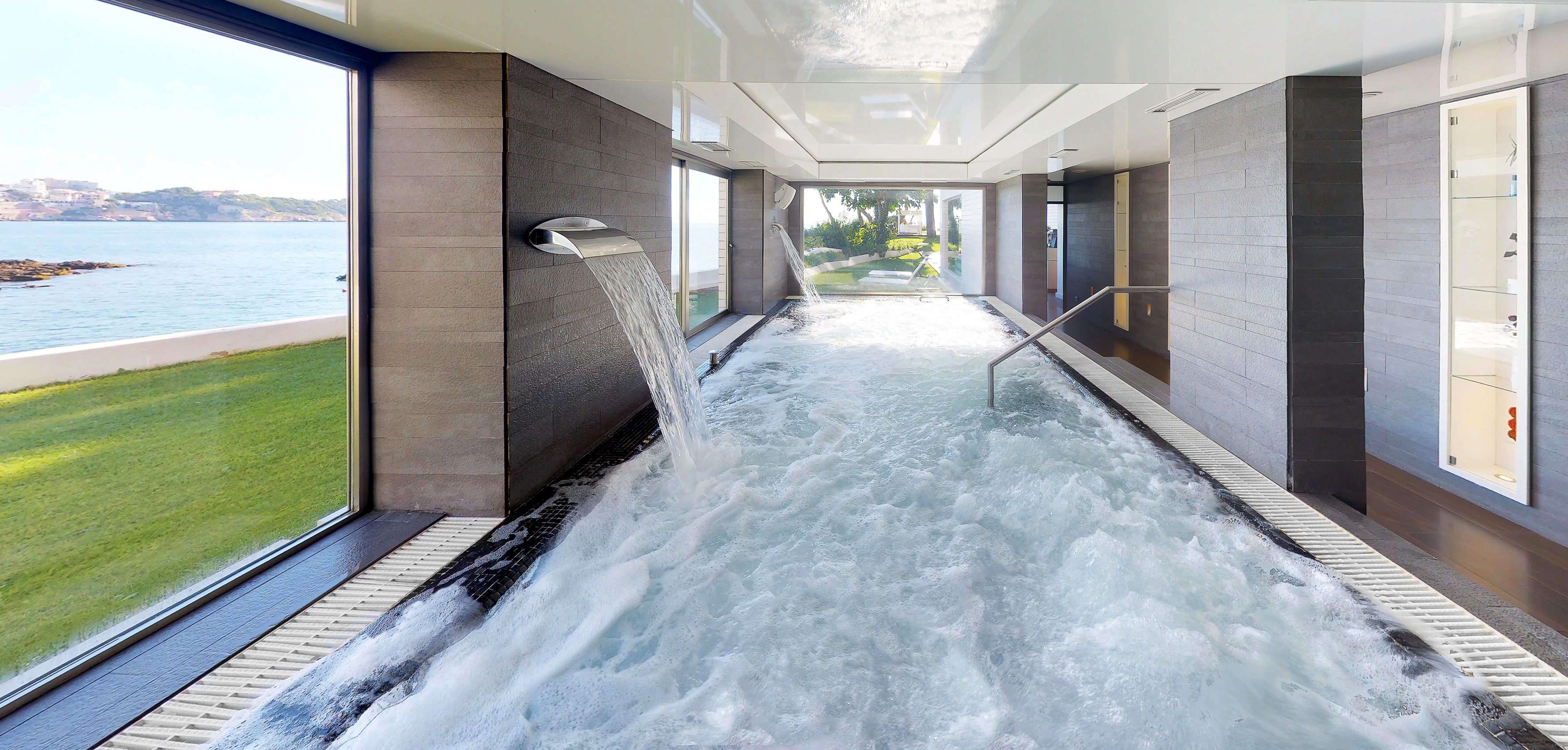 Indoor luxury spa pool with bubbling waterfall, ocean views, and modern design.