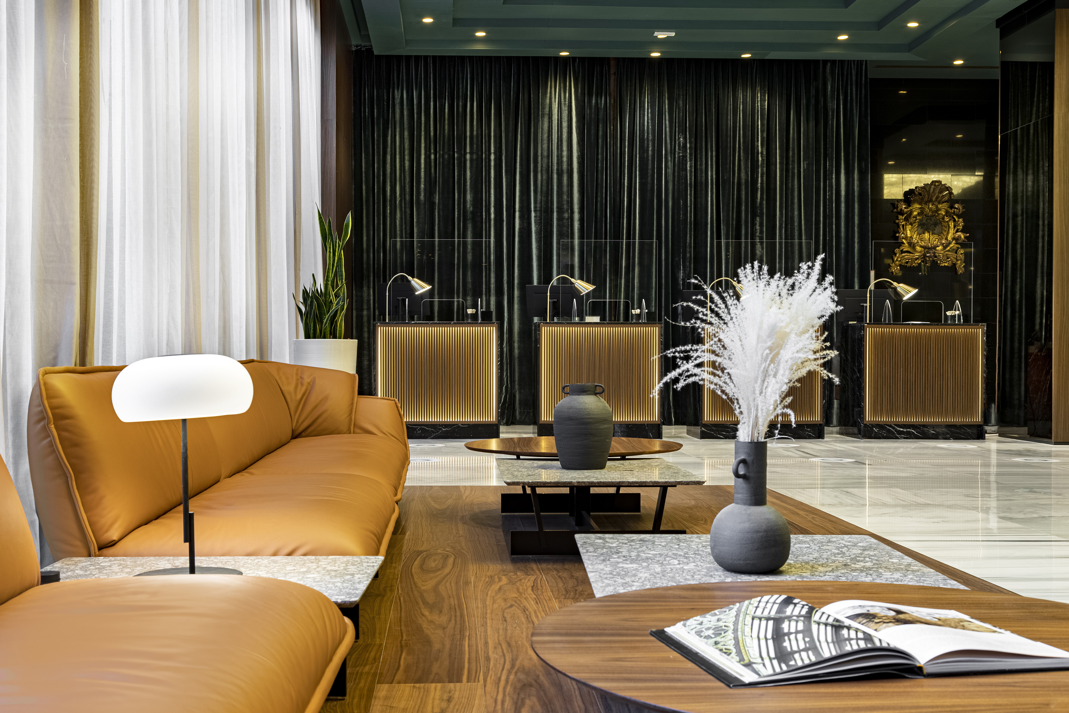 Modern hotel lobby with tan sofas, coffee tables, and backlit reception desks.