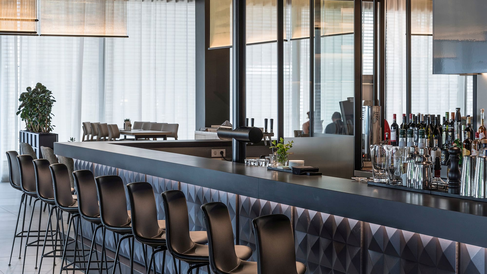 a bar with chairs and a row of bottles