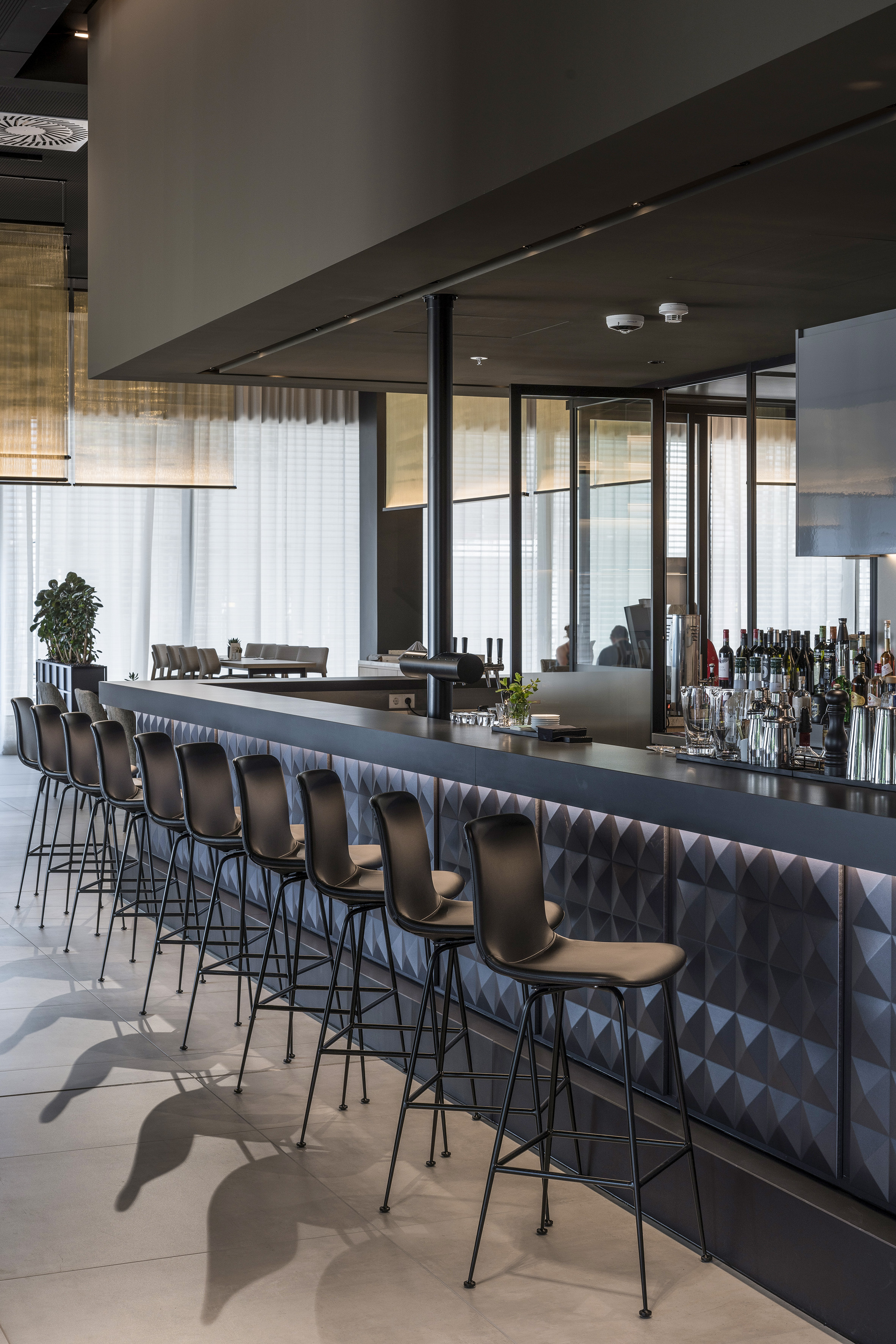 Modern bar with sleek black stools, geometric front, and bottles.