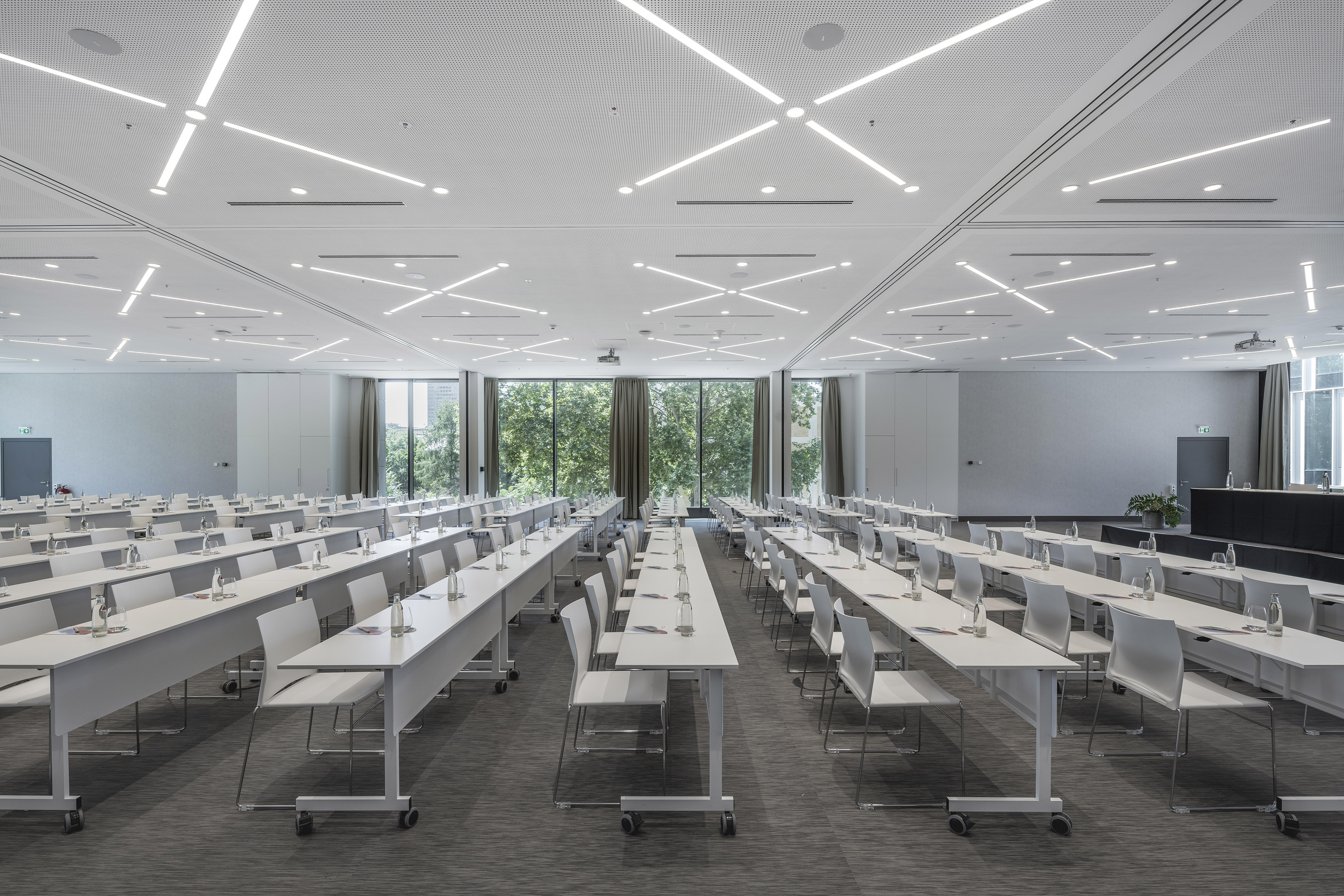 Bright conference room with rows of white tables, chairs, and large windows.