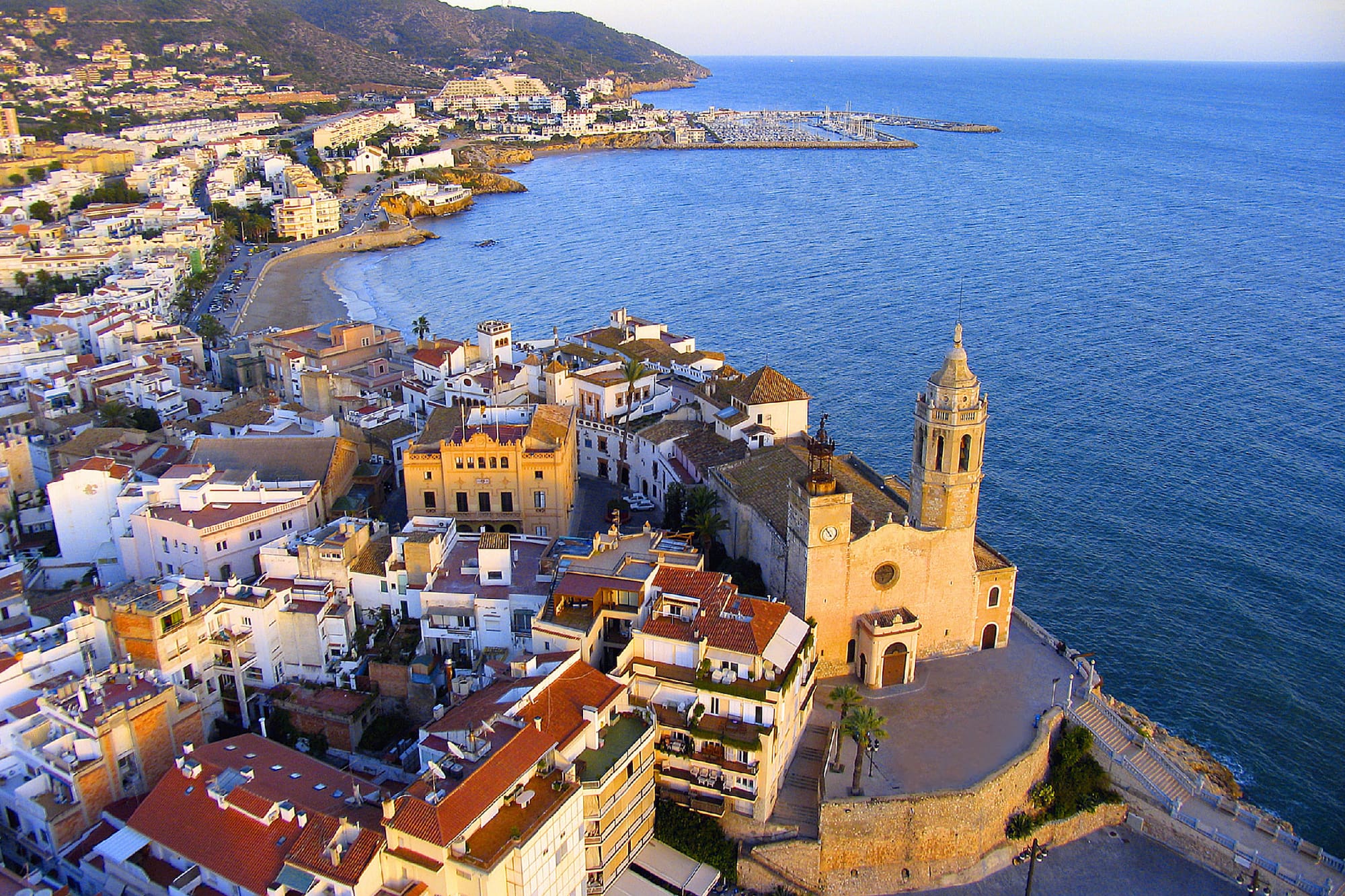 Vista aérea de Sitges con iglesia, pueblo costero, playa y mar Mediterráneo.