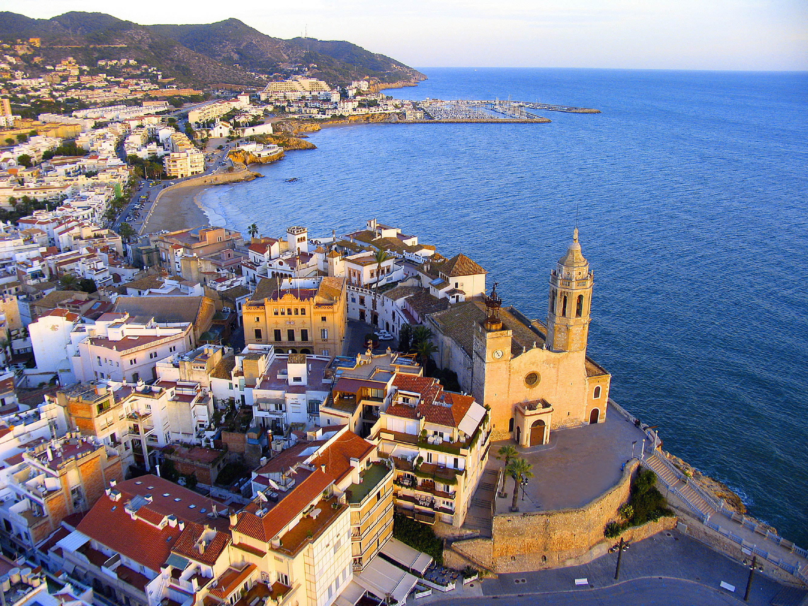 Vista aérea de Sitges con iglesia, pueblo costero, playa y mar Mediterráneo.