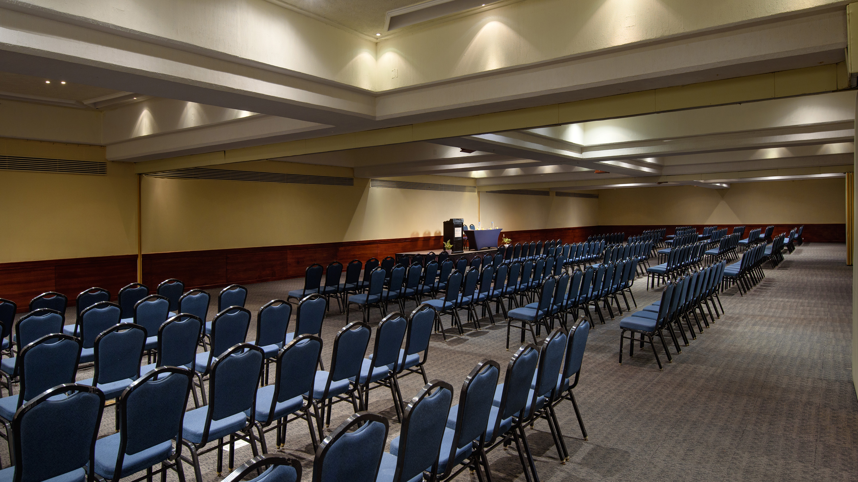 Empty conference room with rows of blue chairs, podium, and presentation area.
