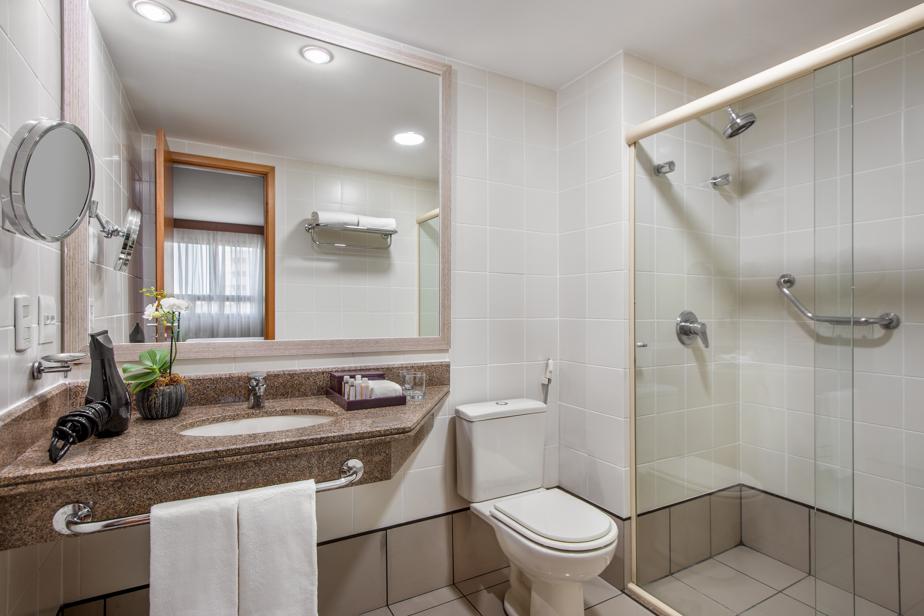 Modern hotel bathroom with granite vanity, sink, mirror, toilet, and glass shower.