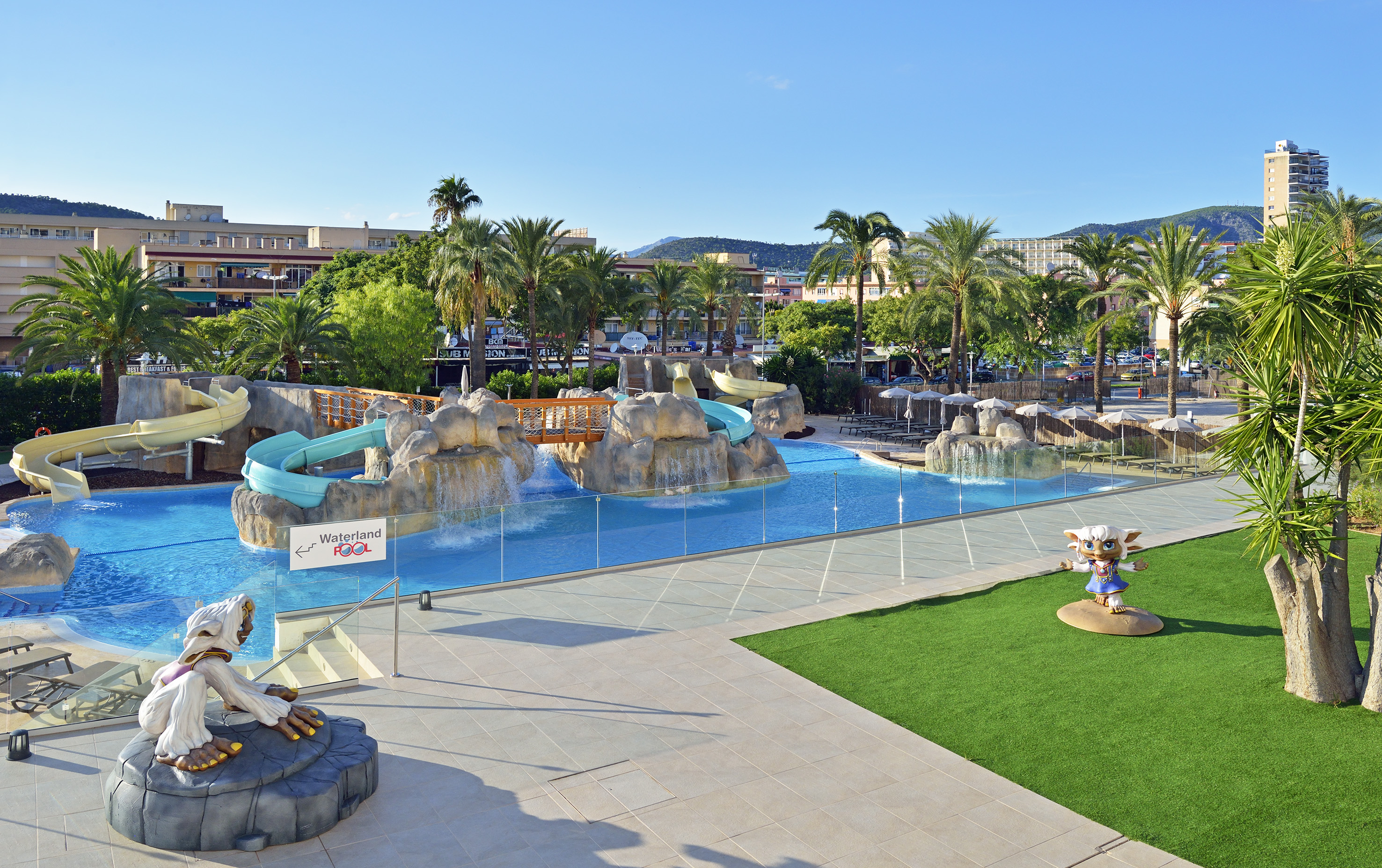 Waterland Pool at a resort: blue slides, rock waterfalls, palm trees, hotel.