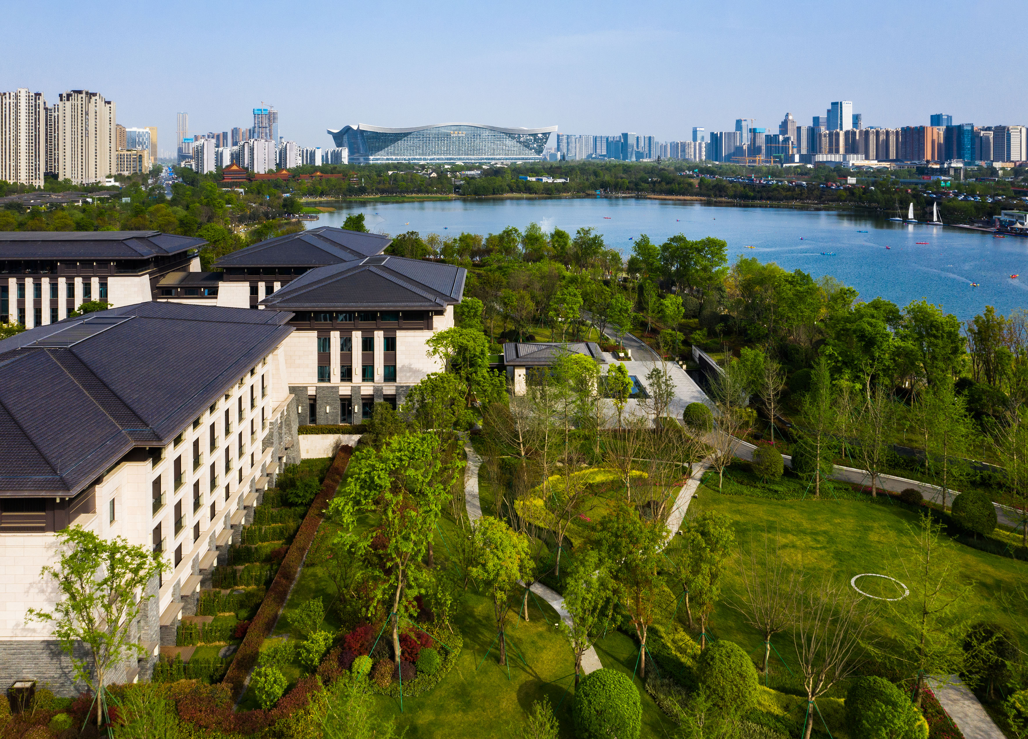 Lush resort gardens, traditional buildings, lake with boats, city skyline.