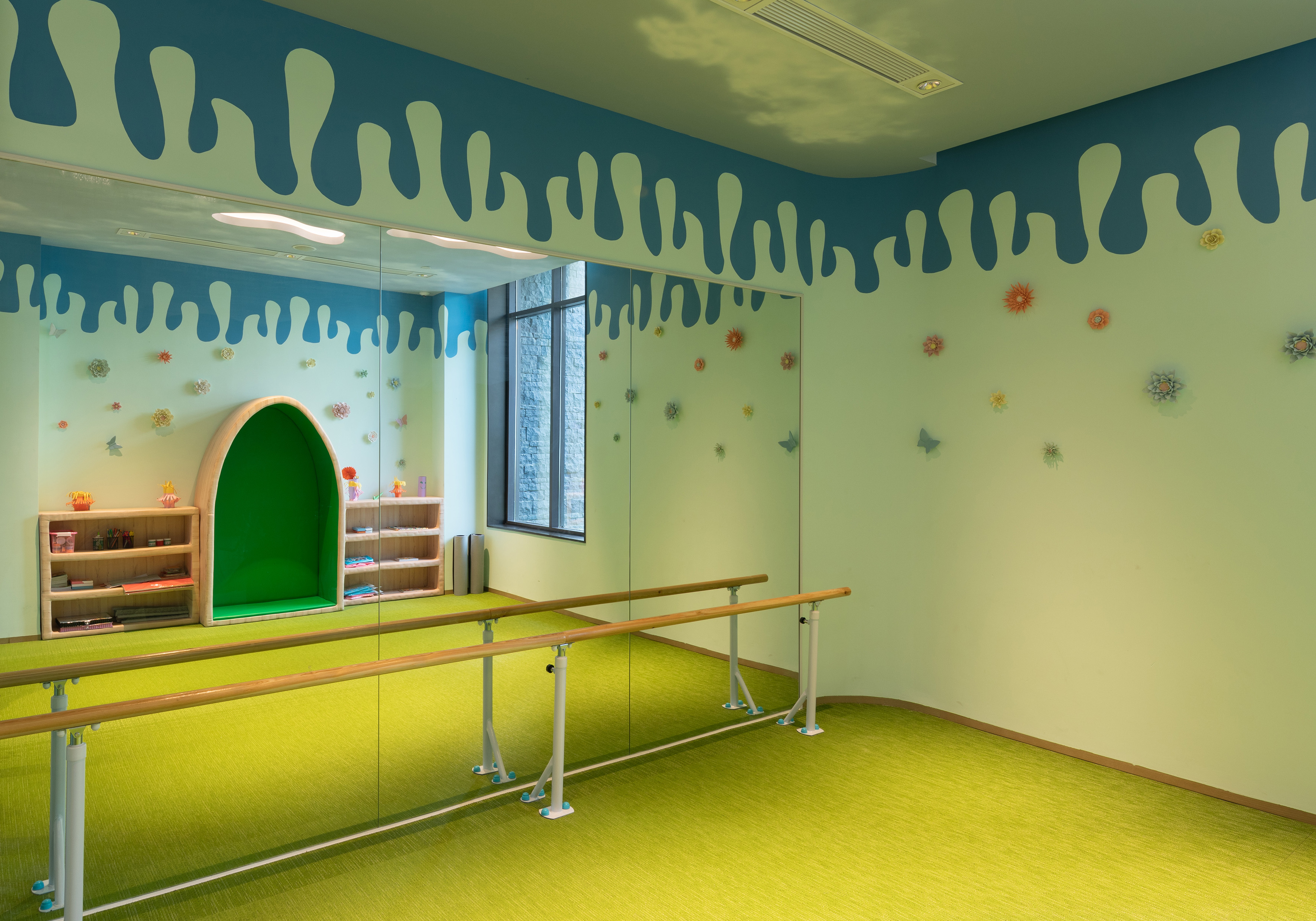 Kids' dance studio with green carpet, mirror wall, ballet barres, and colorful wall decor.