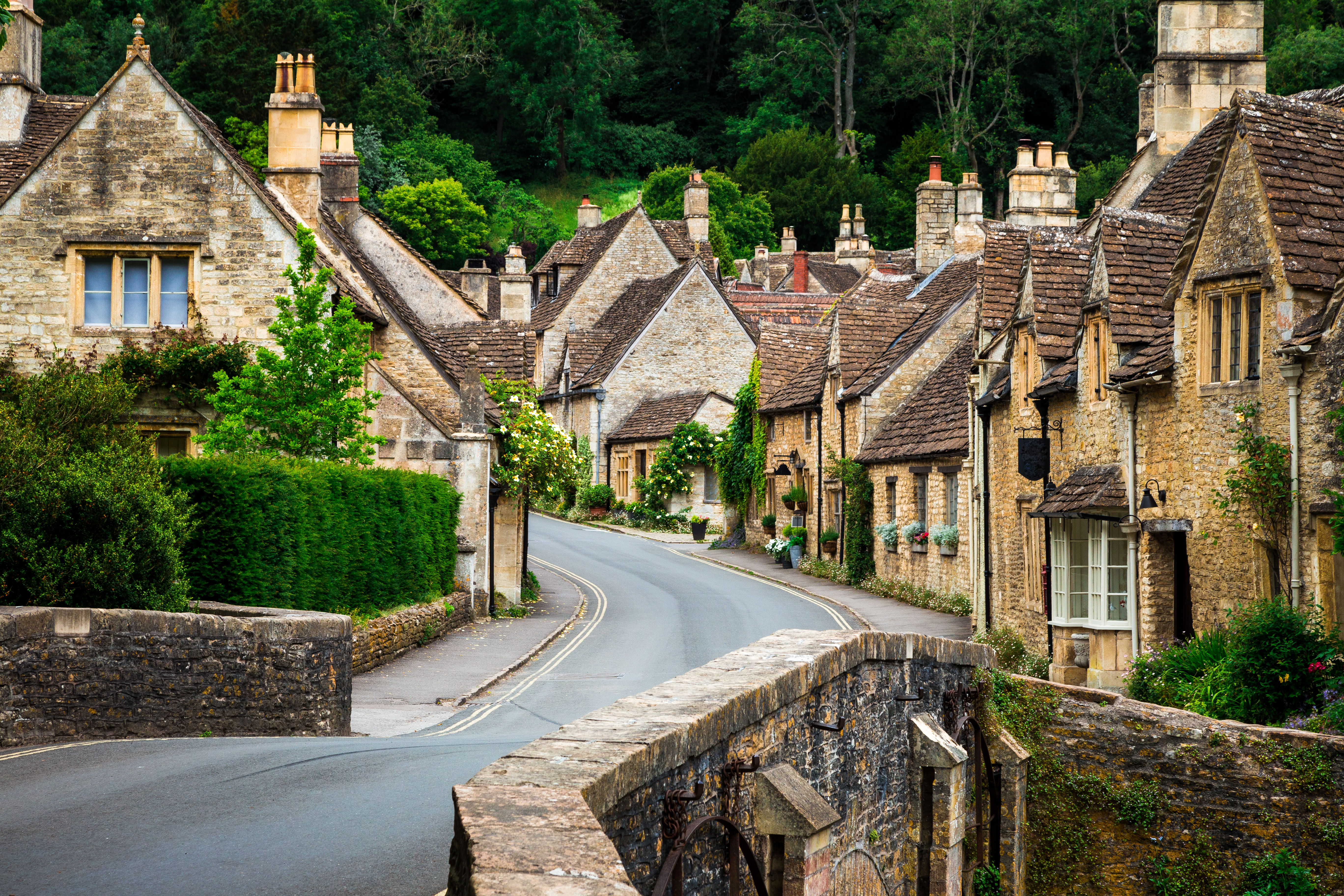 a road between houses with trees with Cotswolds in the background