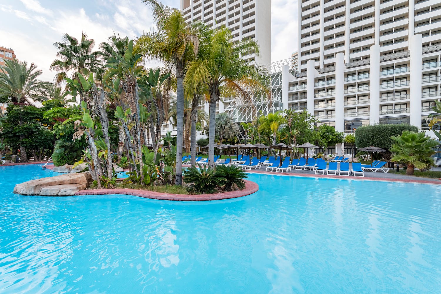 a pool with palm trees and chairs in front of a building
