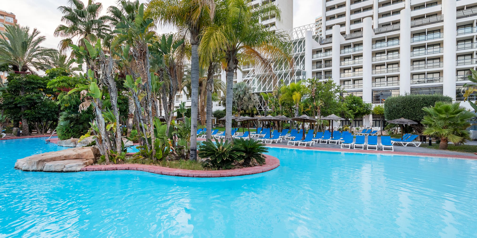 a pool with palm trees and chairs in front of a building
