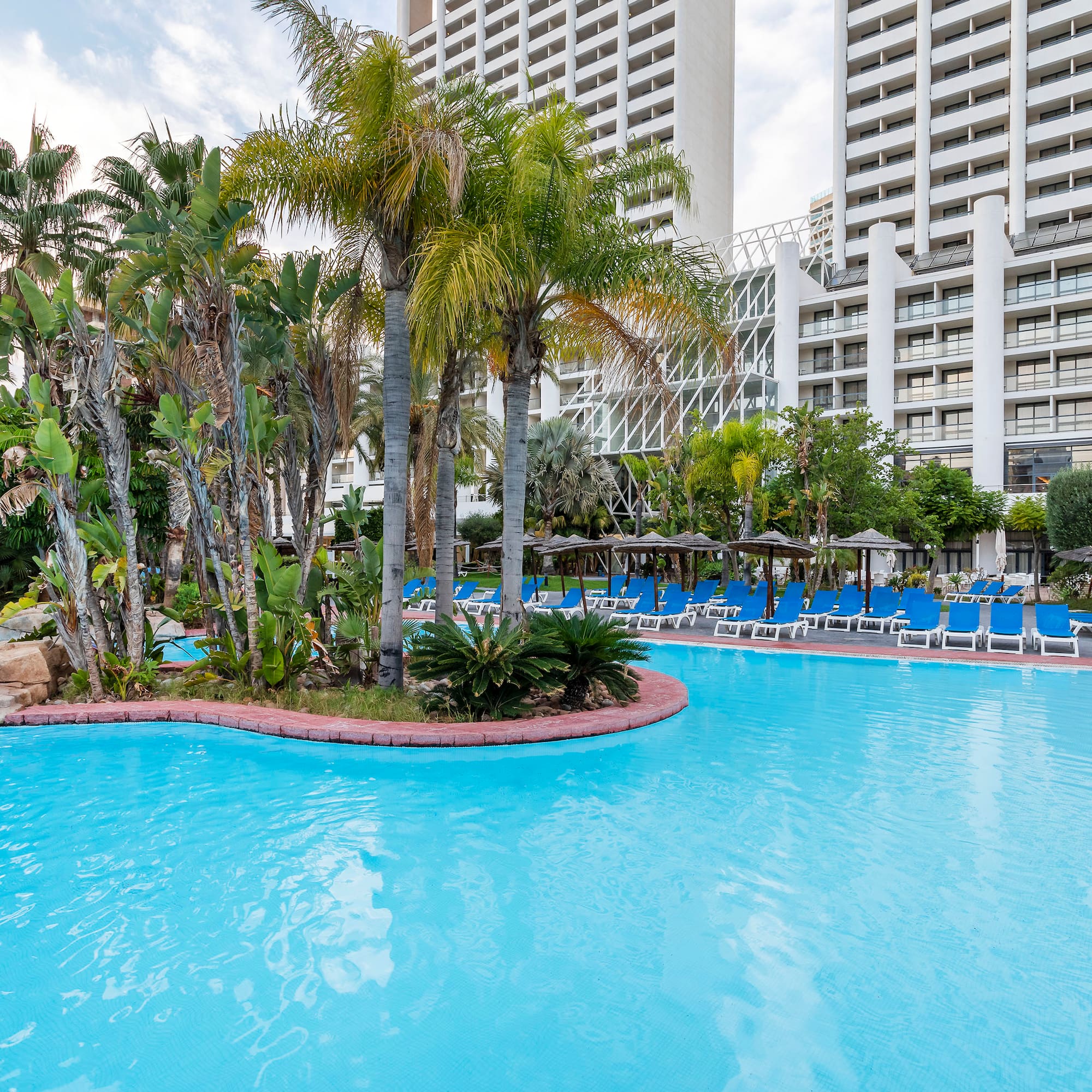 a pool with palm trees and chairs in front of a building