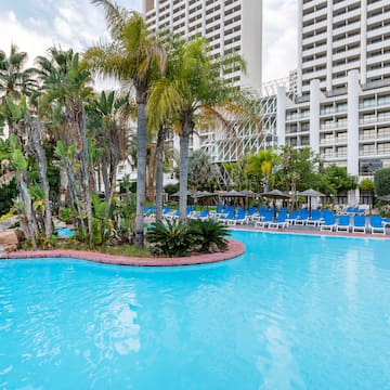a pool with palm trees and chairs in front of a building