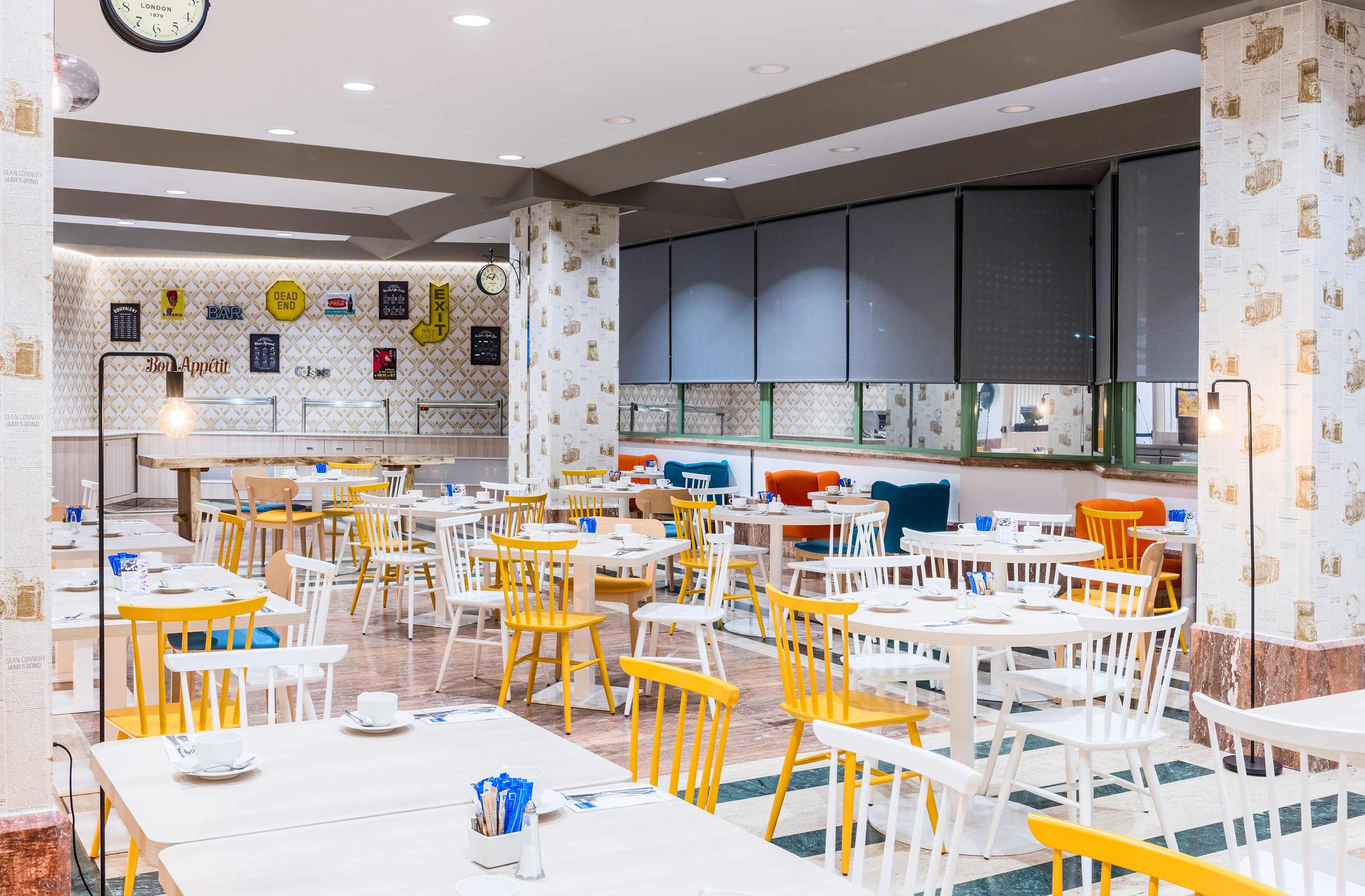 Modern, bright hotel breakfast room with white and yellow seating, buffet.