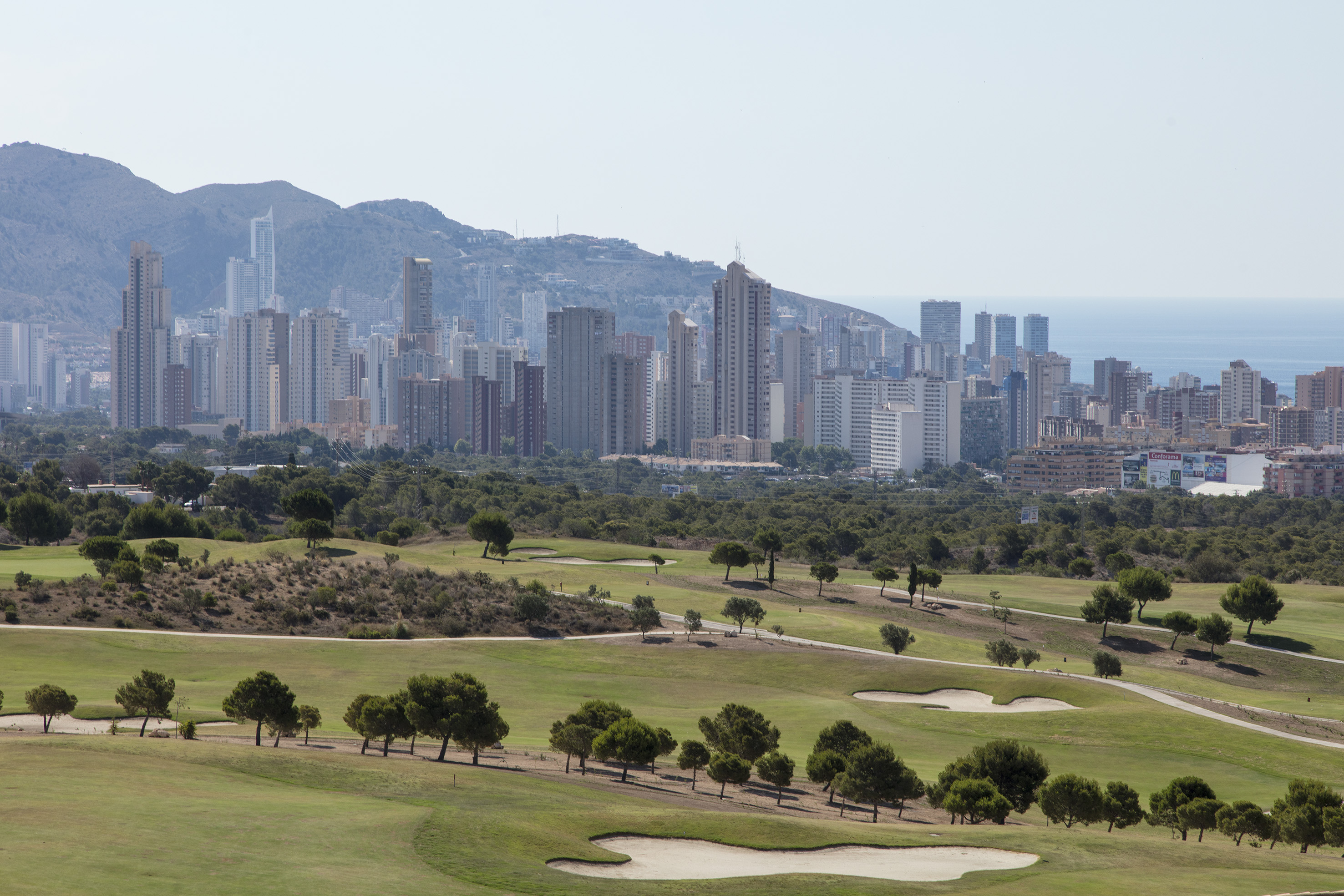 Coastal golf course with cityscape, mountains, and ocean view.