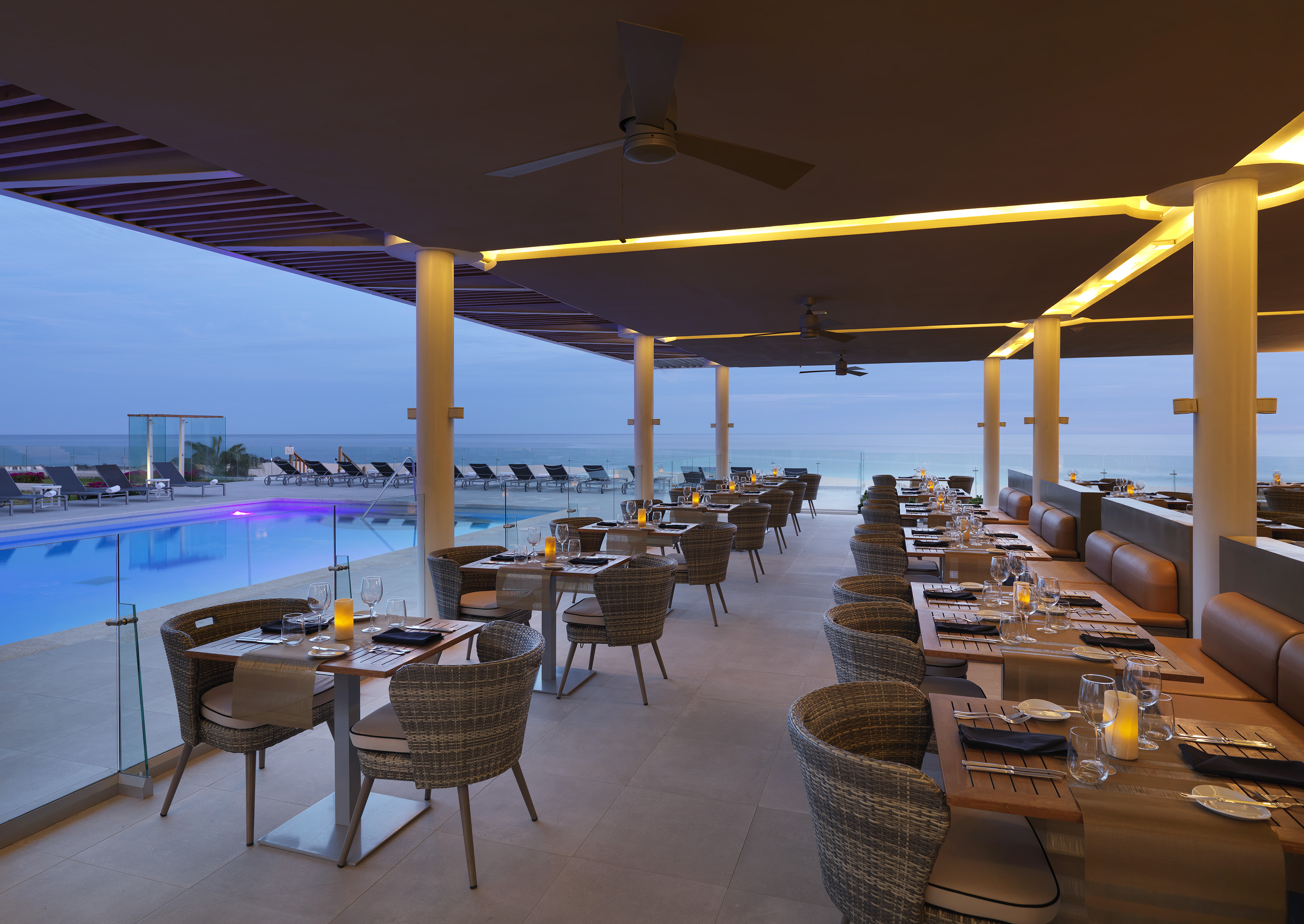 Oceanfront resort restaurant patio at dusk with set tables, pool, and sea view.