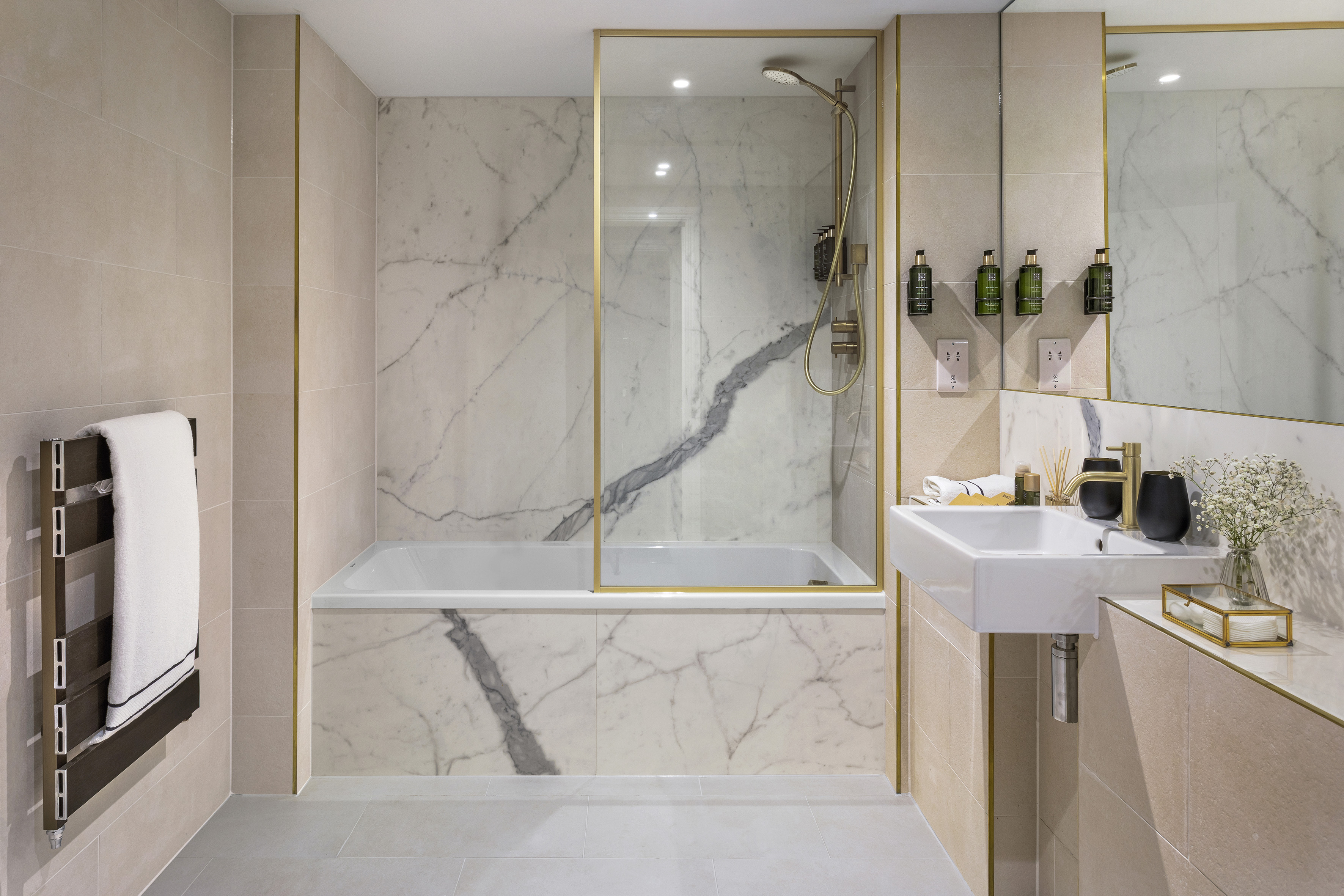 Modern luxury bathroom with marble walls, gold accents, shower-bath, and sink.