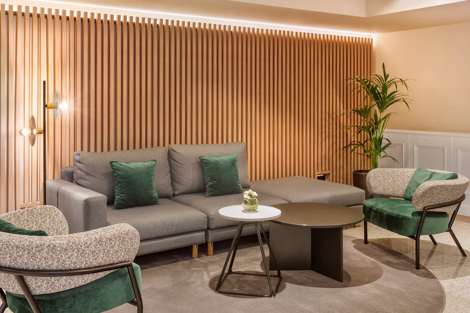 Modern lounge with grey sectional sofa, green armchairs, and wooden slatted wall.