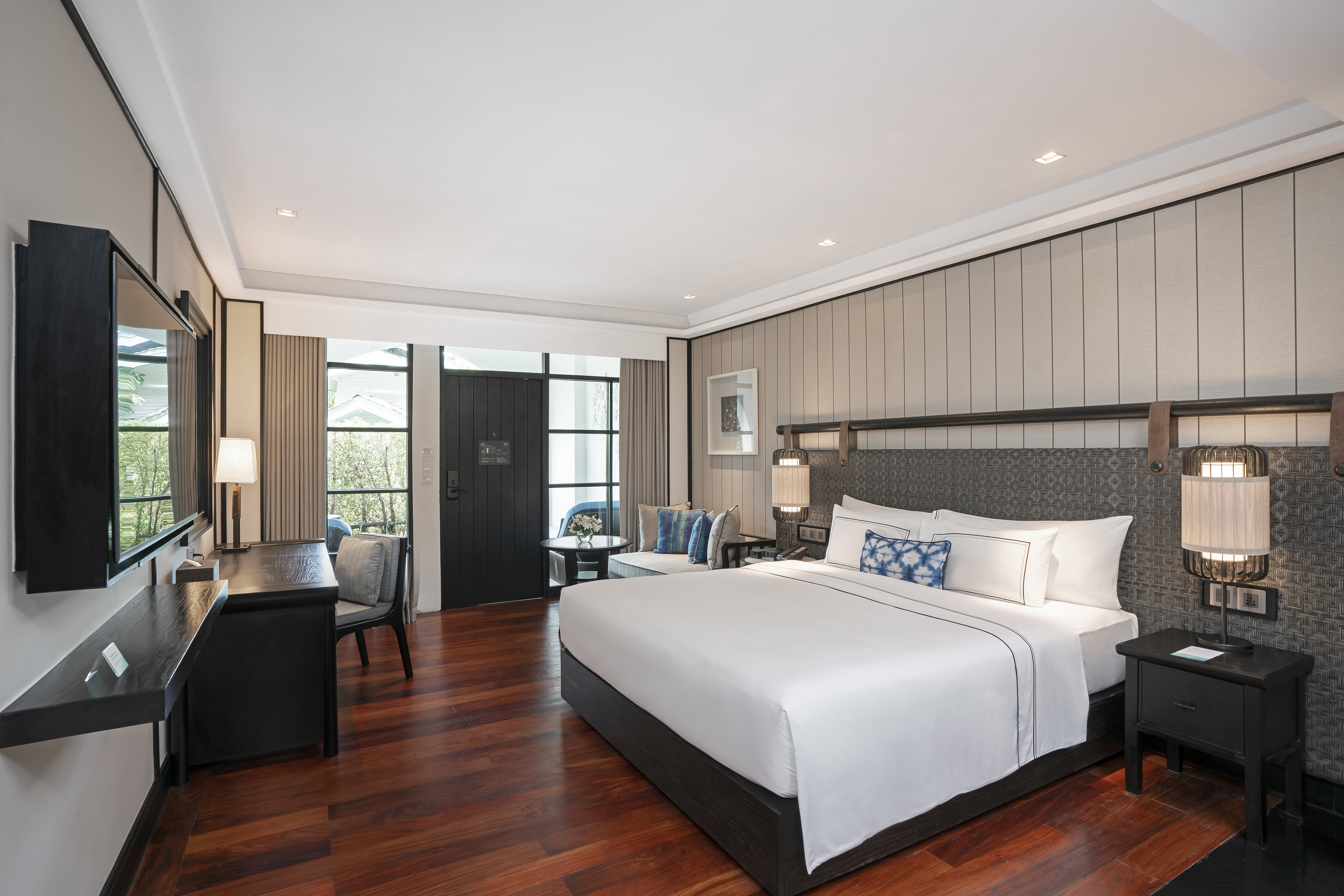 Luxury hotel room with large bed, desk, warm wooden floor, and bright windows.