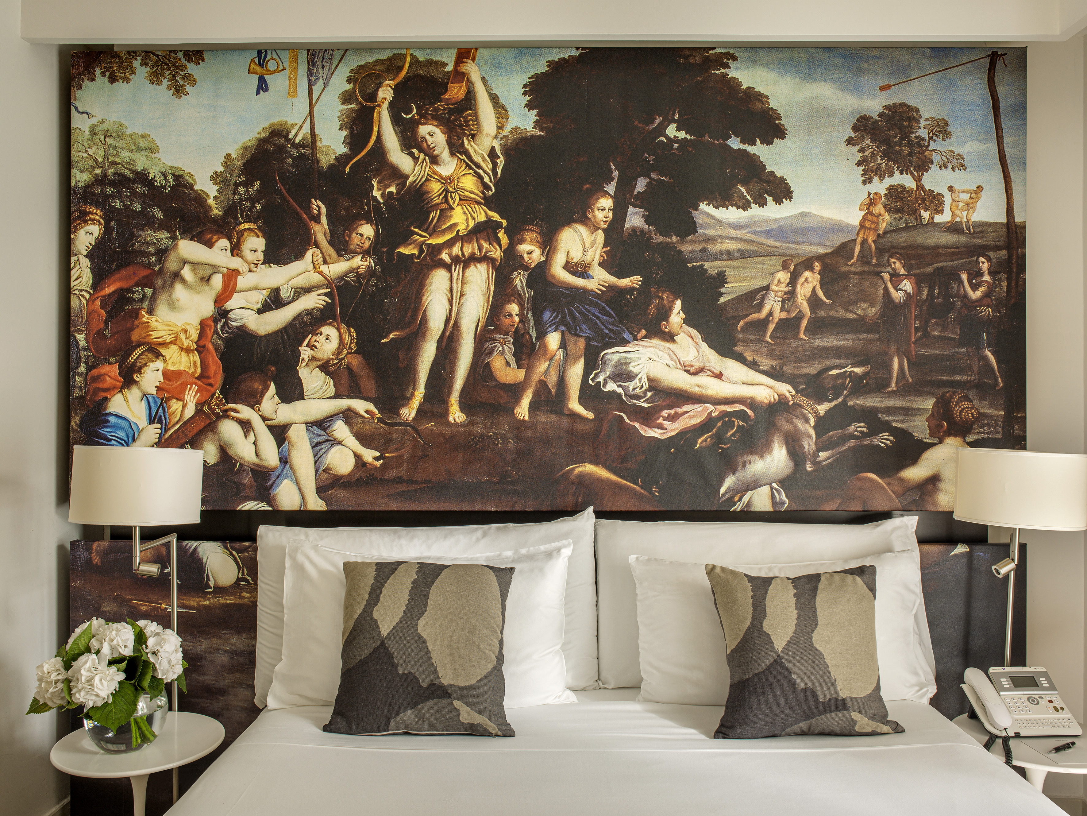 Hotel bed with classical mural headboard, white bedding, decorative pillows.