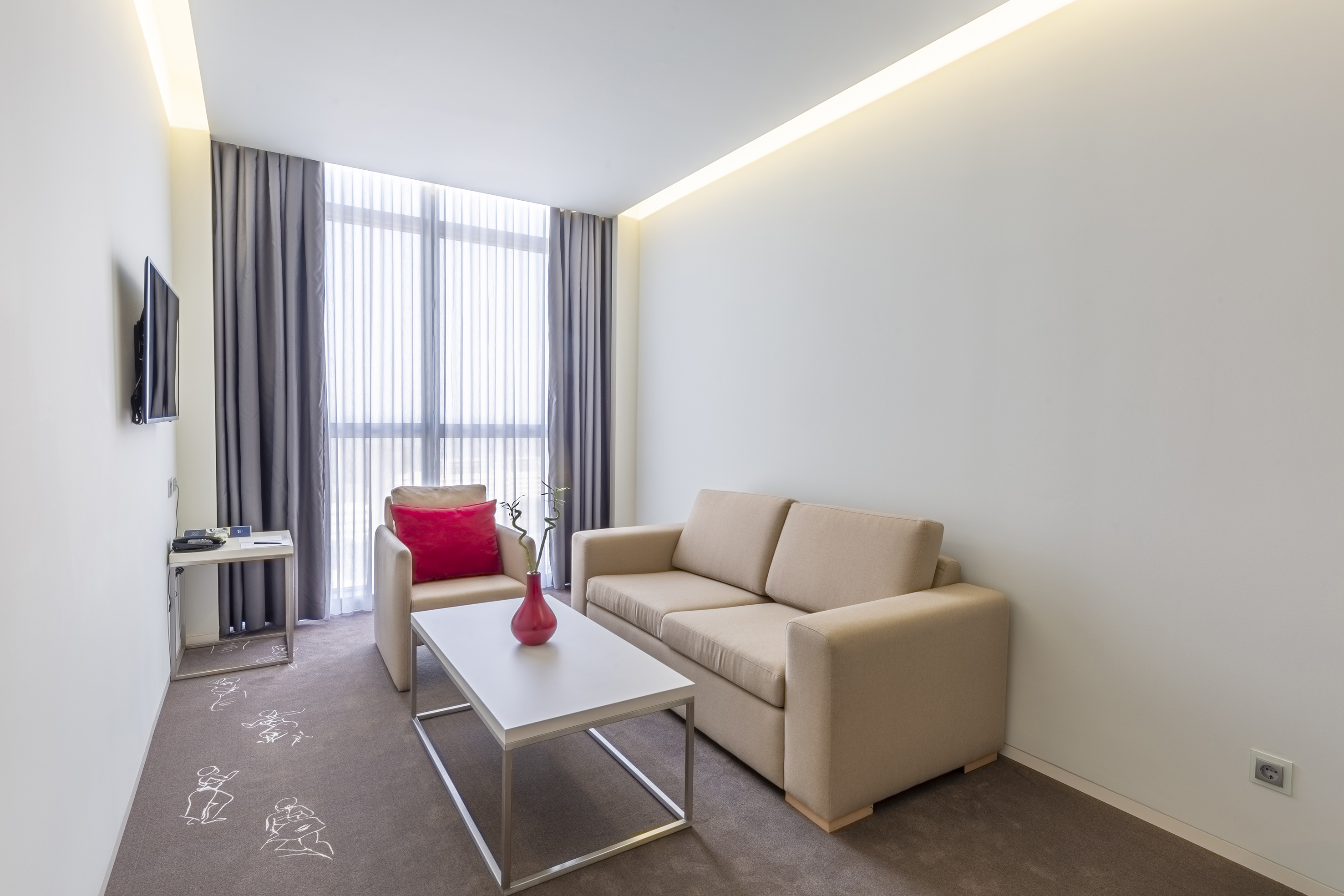 Modern hotel living room with beige sofa, armchair, coffee table, and window.