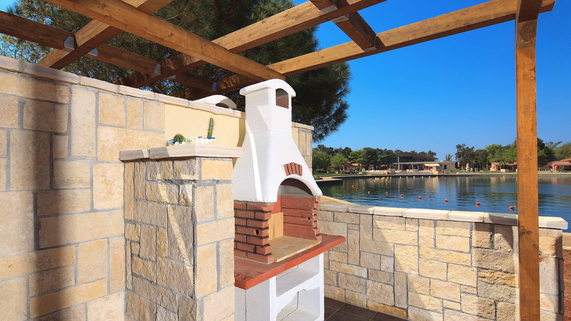 a stone patio with a wood roof over a lake