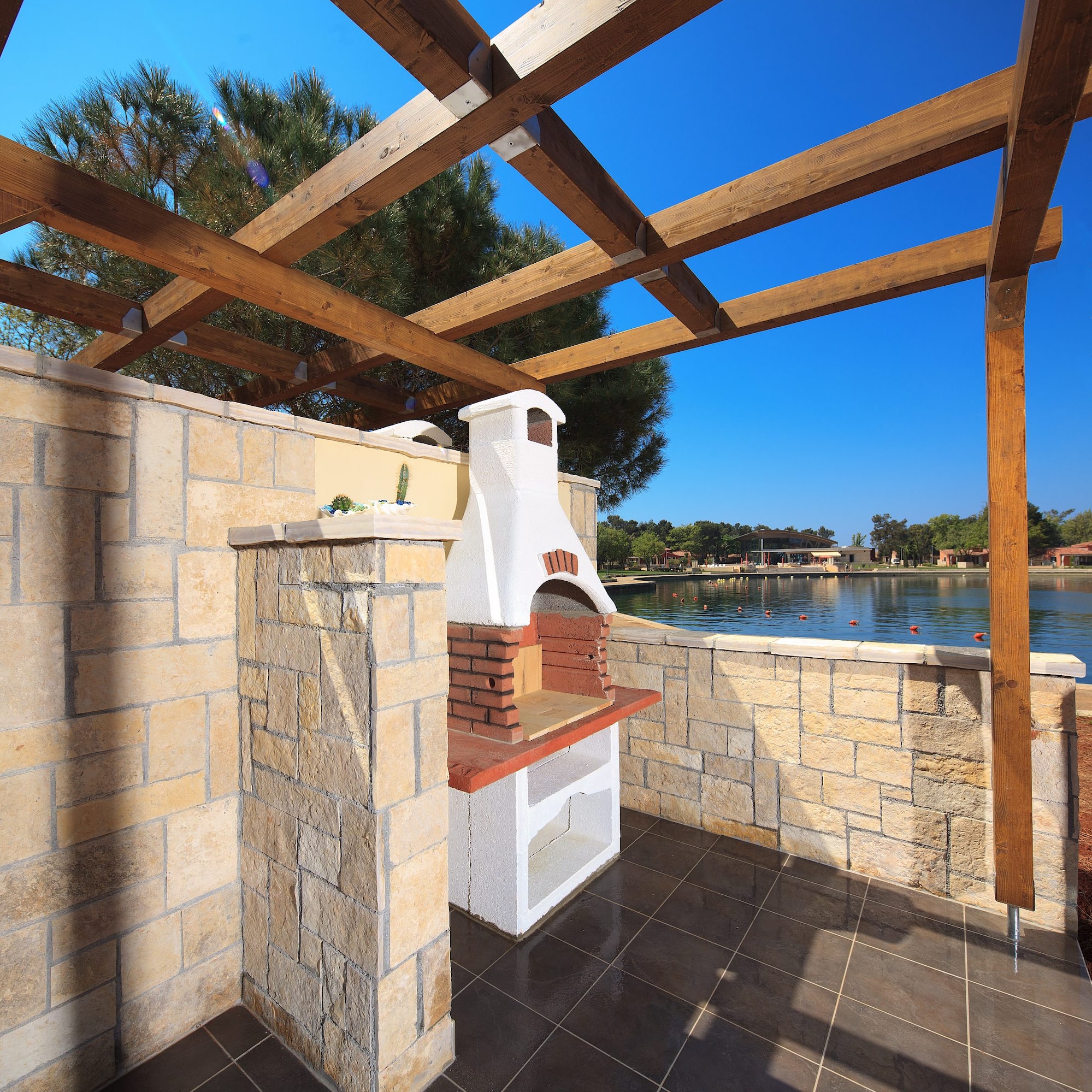 a stone patio with a wood roof over a lake