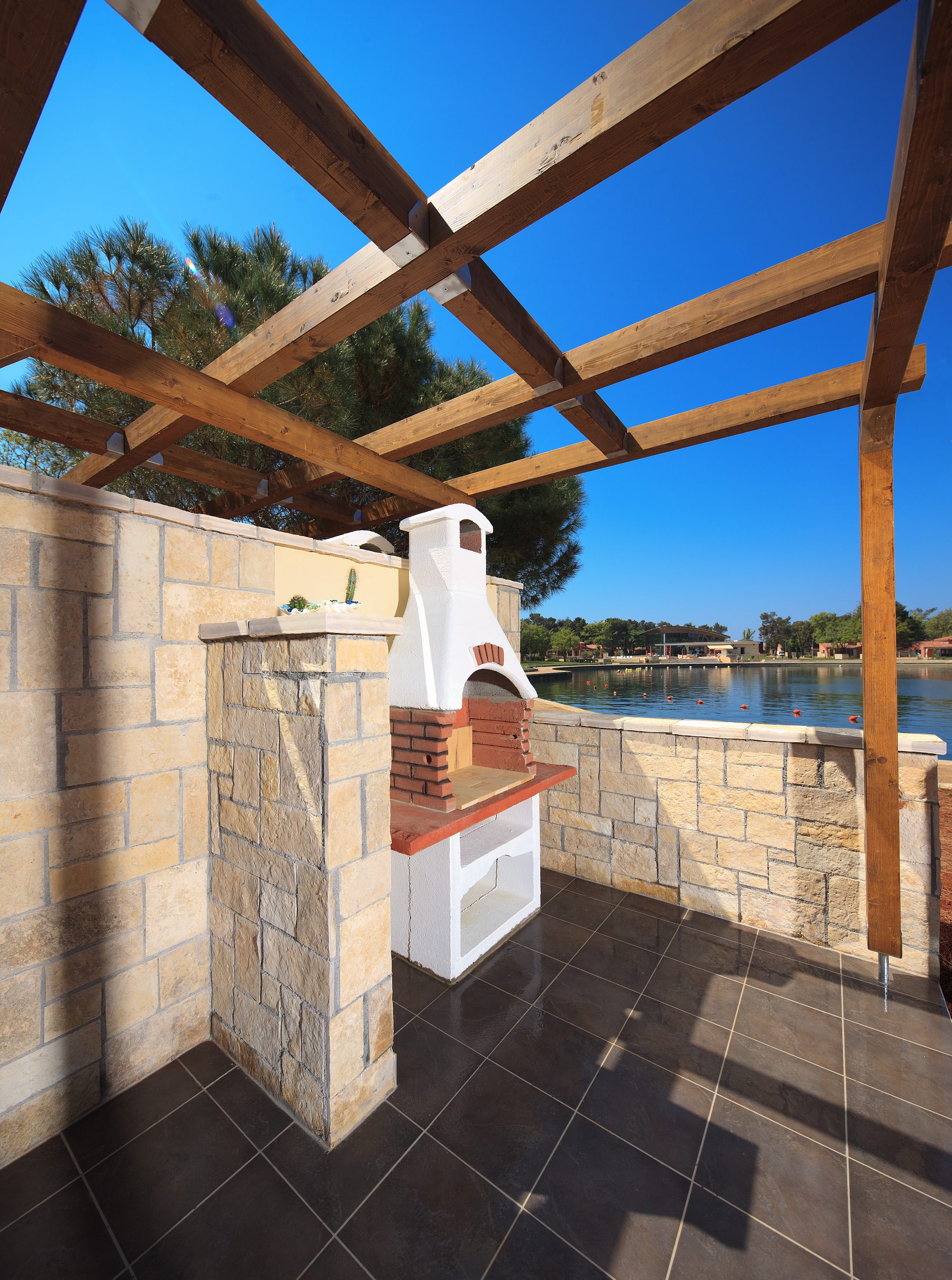 a stone patio with a wood roof over a lake