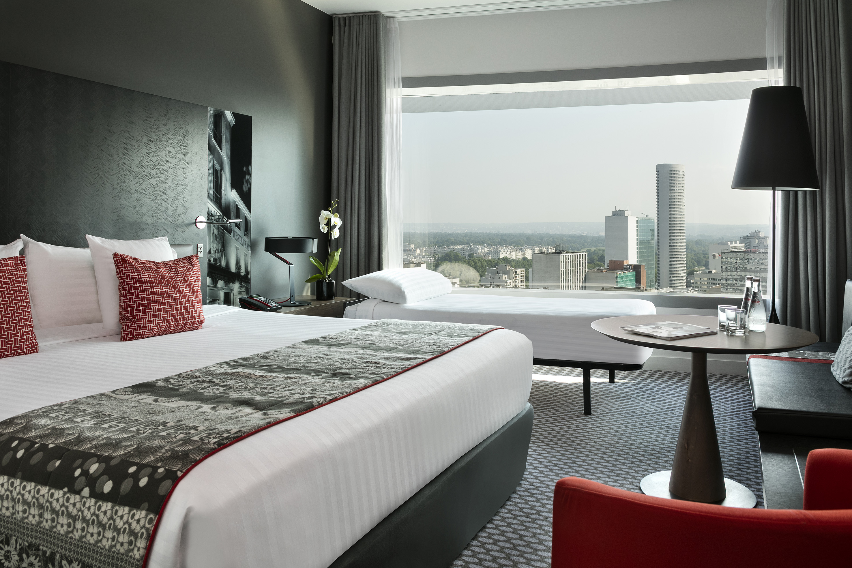 Modern hotel room with city skyline view, large bed, and sofa bed.