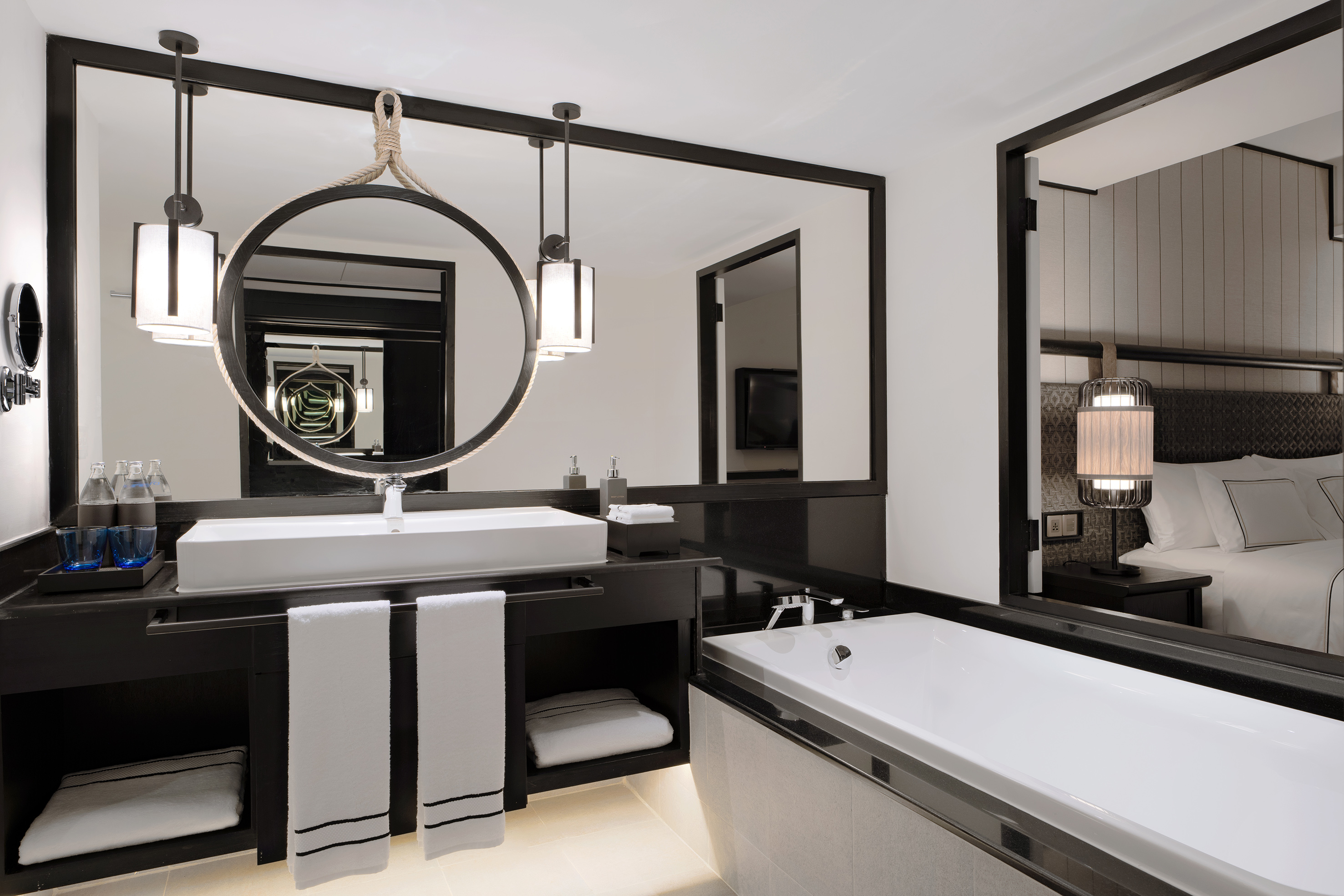 Luxury bathroom with round mirror, white sink, bathtub, and black vanity.
