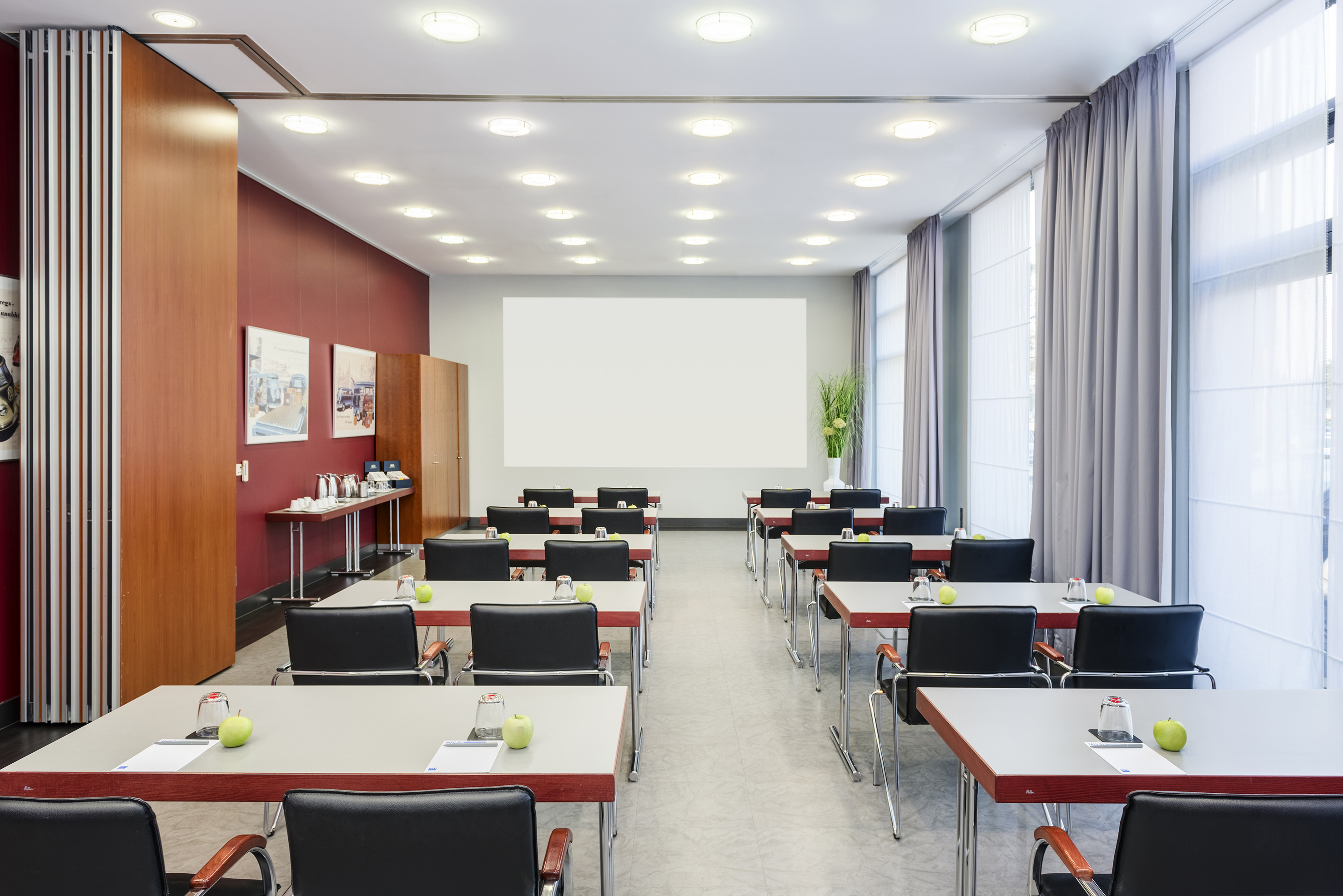 Modern conference room with tables, black chairs, large screen, and green apples.