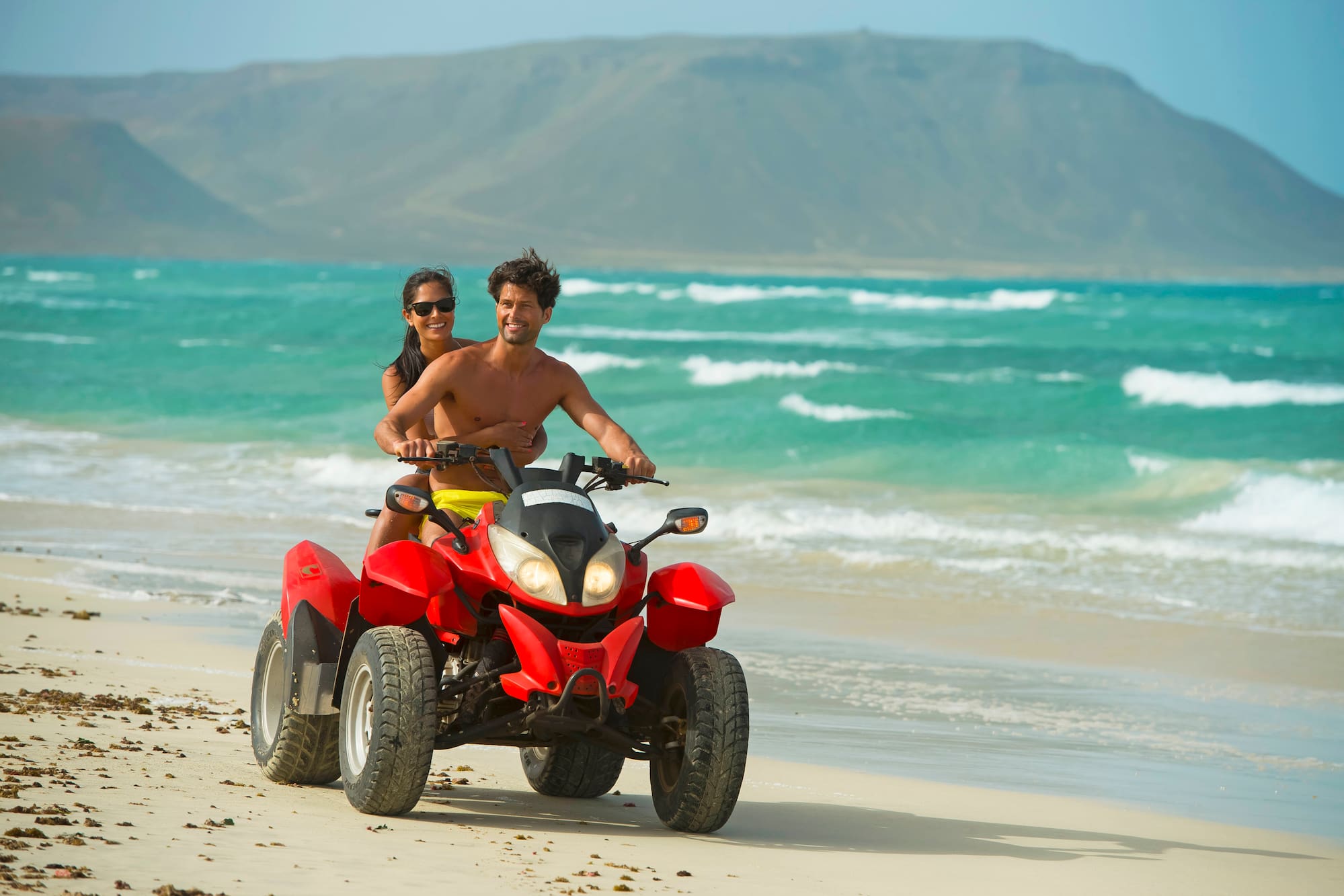 a man and woman on a quad bike on a beach