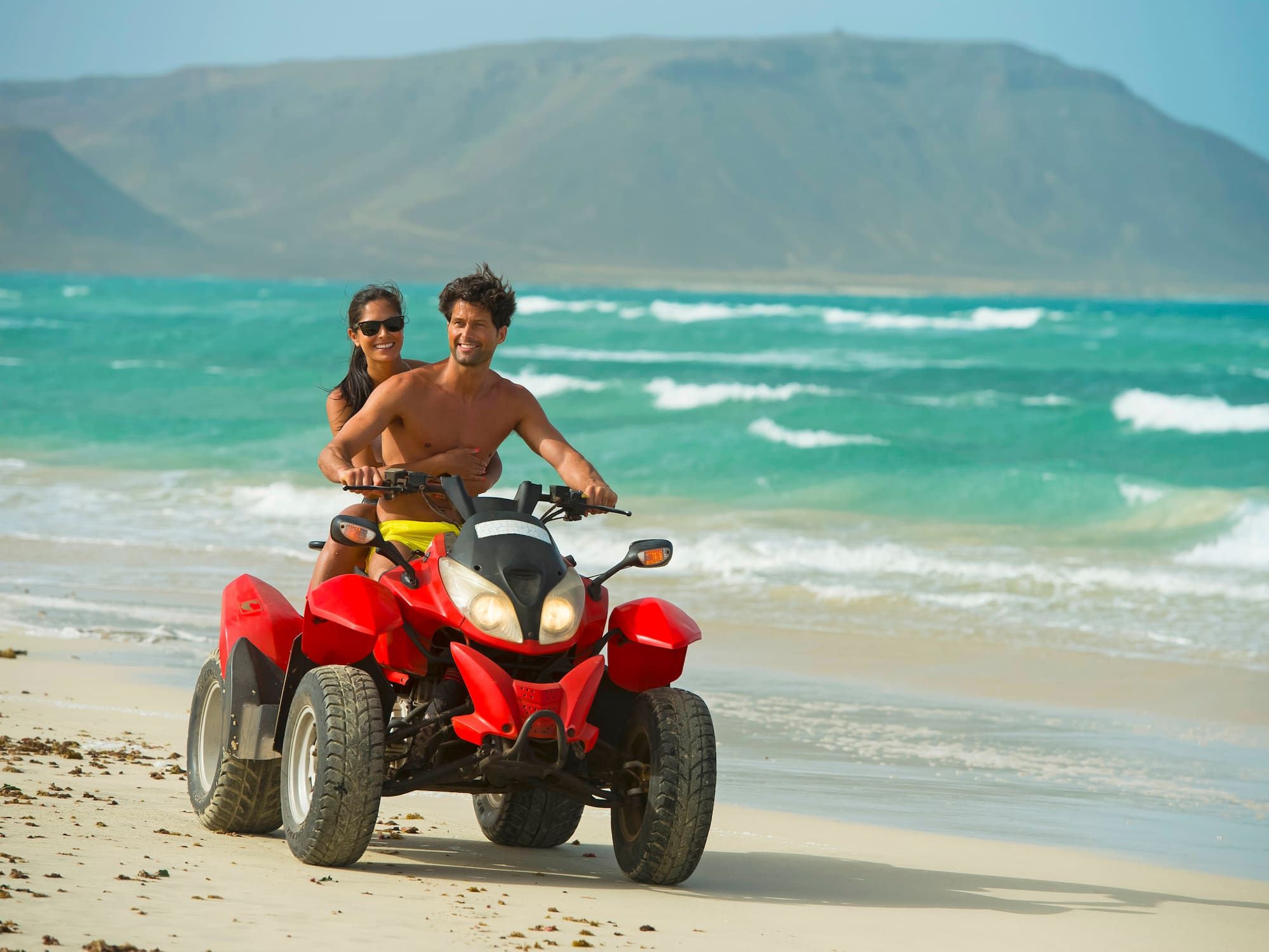 a man and woman on a quad bike on a beach
