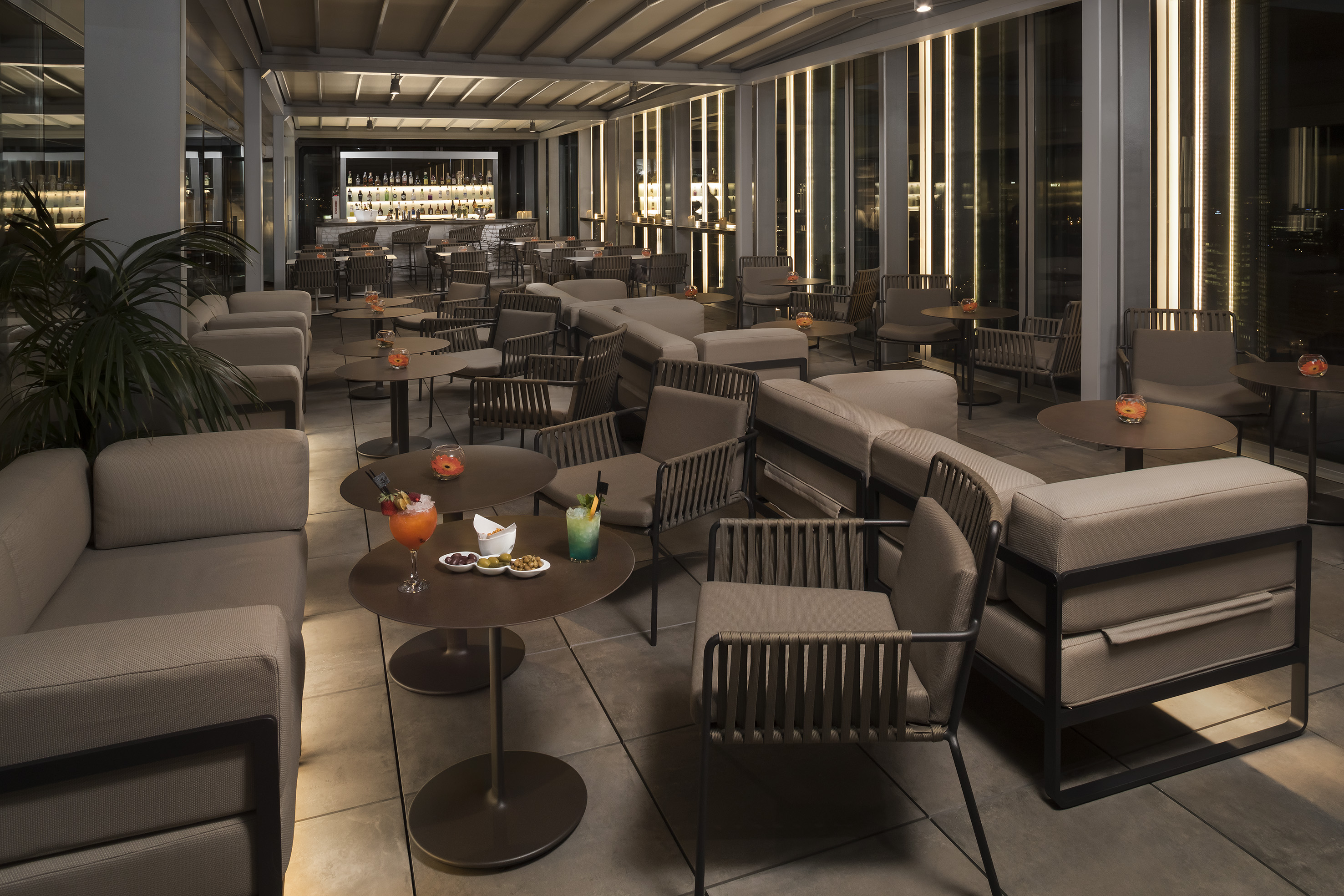 Rooftop bar lounge at night with modern seating, cocktails, and city views.