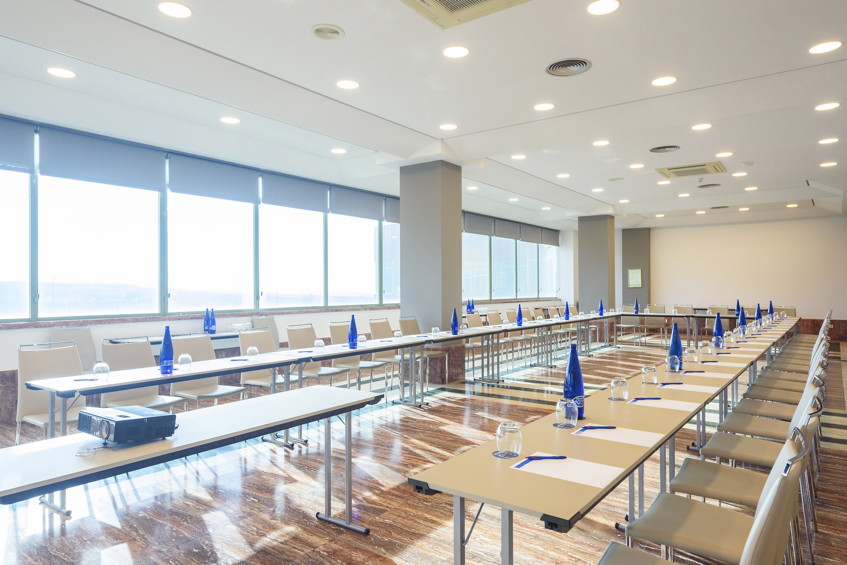 Modern U-shaped conference room with tables, chairs, projector, and large windows.
