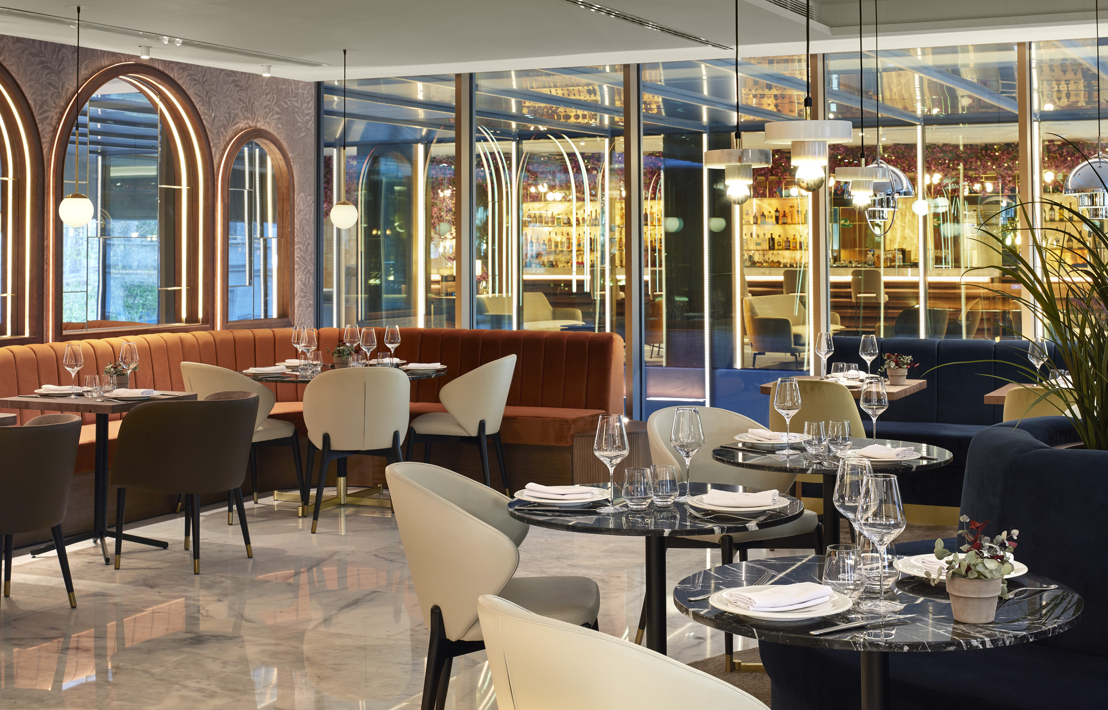 Elegant restaurant interior with set tables, booth seating, bar behind glass.