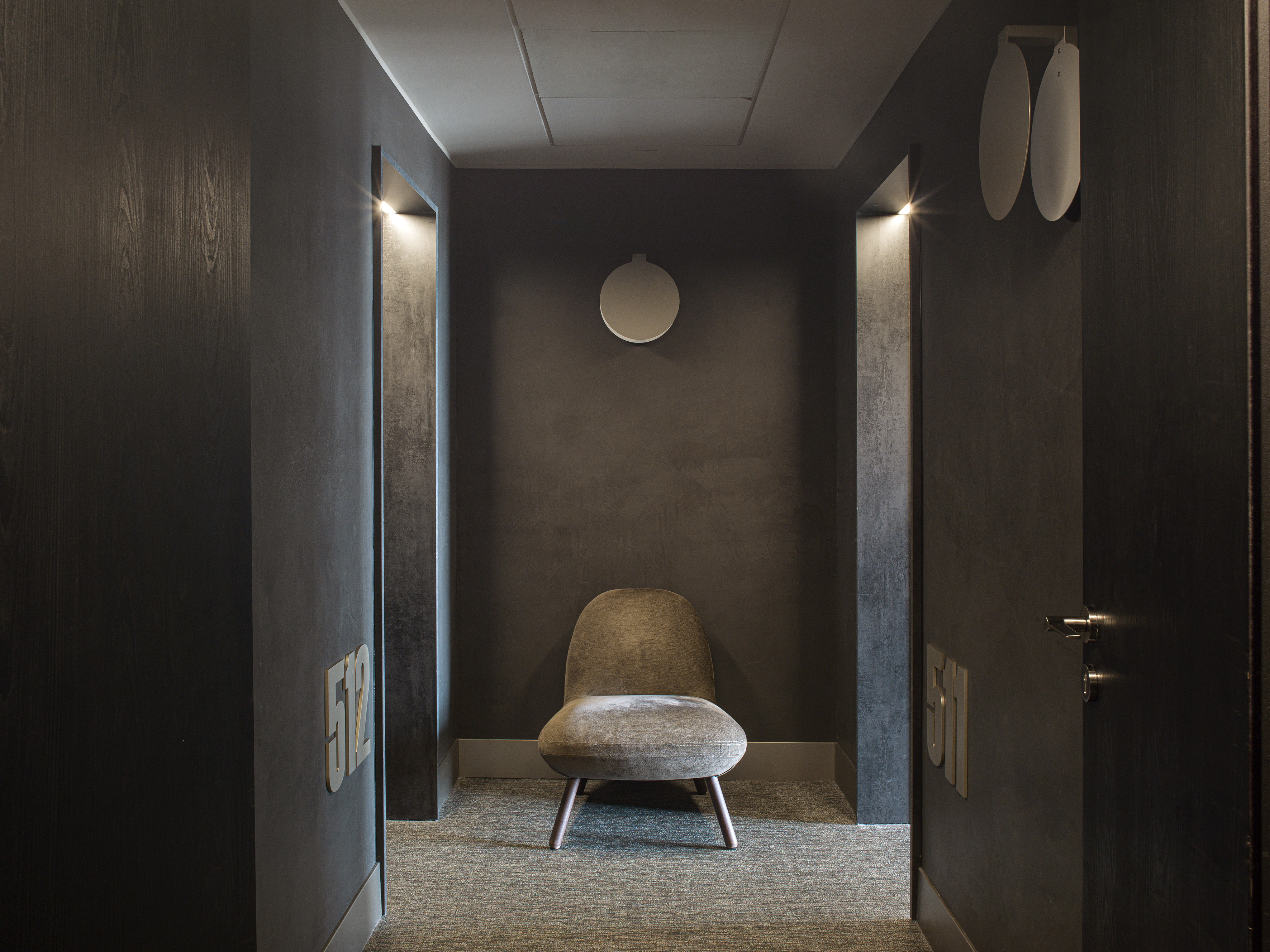 Dark modern hotel hallway with gray upholstered chair, room numbers 511/512.